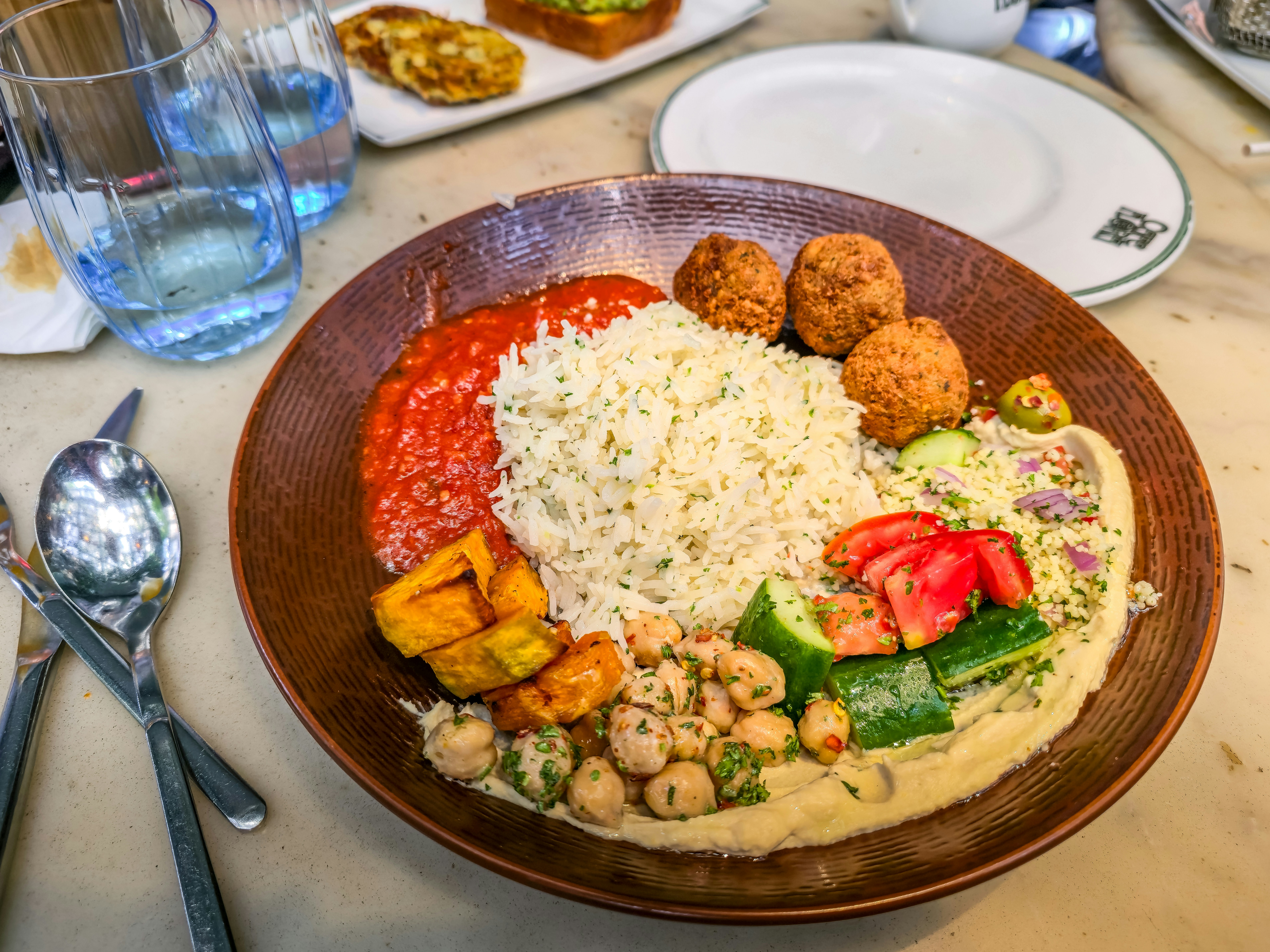 A plate of rice, falafel, hummus, roasted squash, and salad on a table