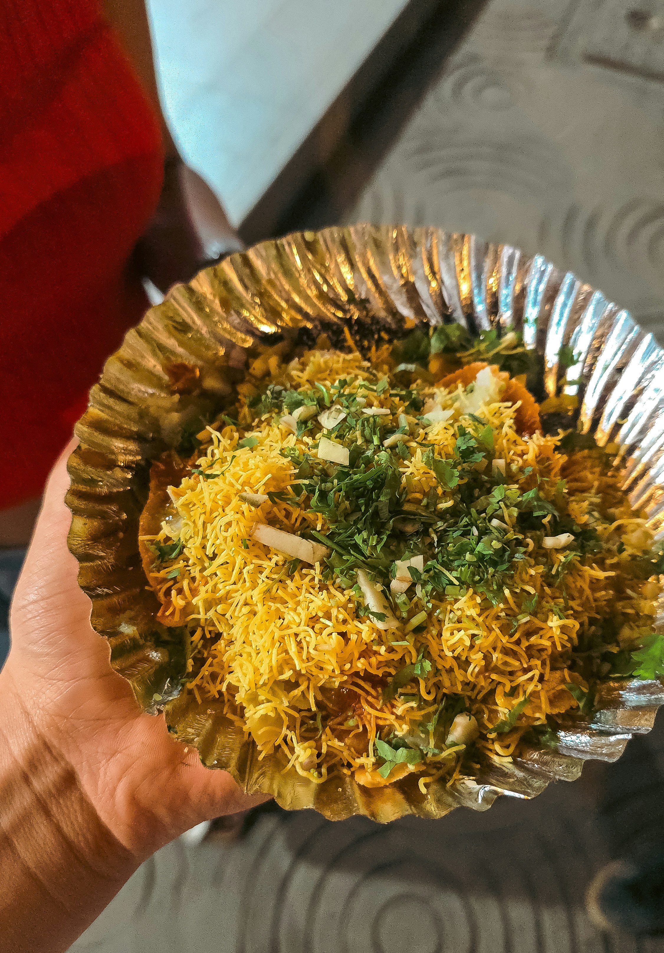 A person holding a foil plate of sev puri topped with fresh cilantro