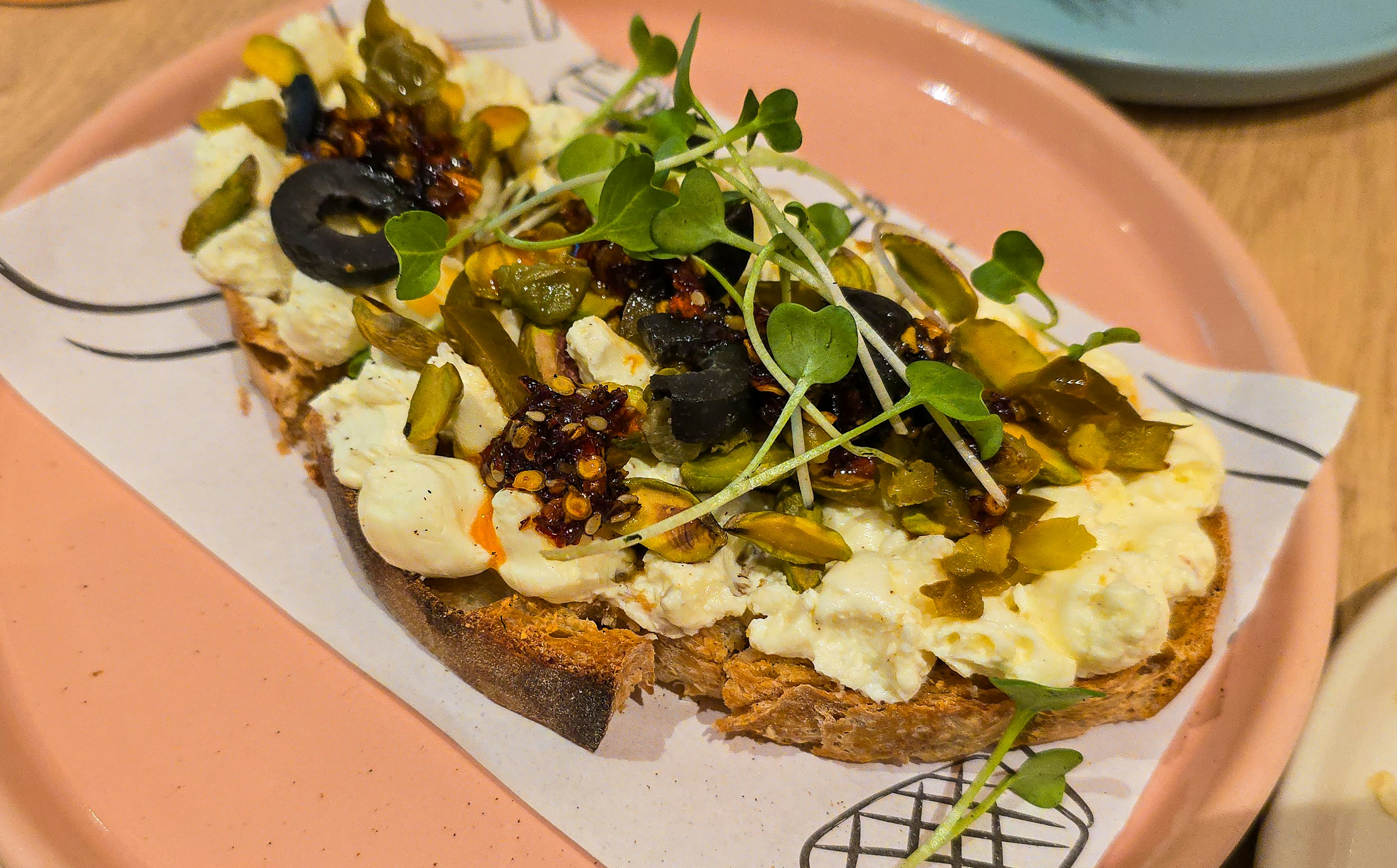 Toasted bread topped with creamy cheese, black olives, pistachios, and fresh microgreens