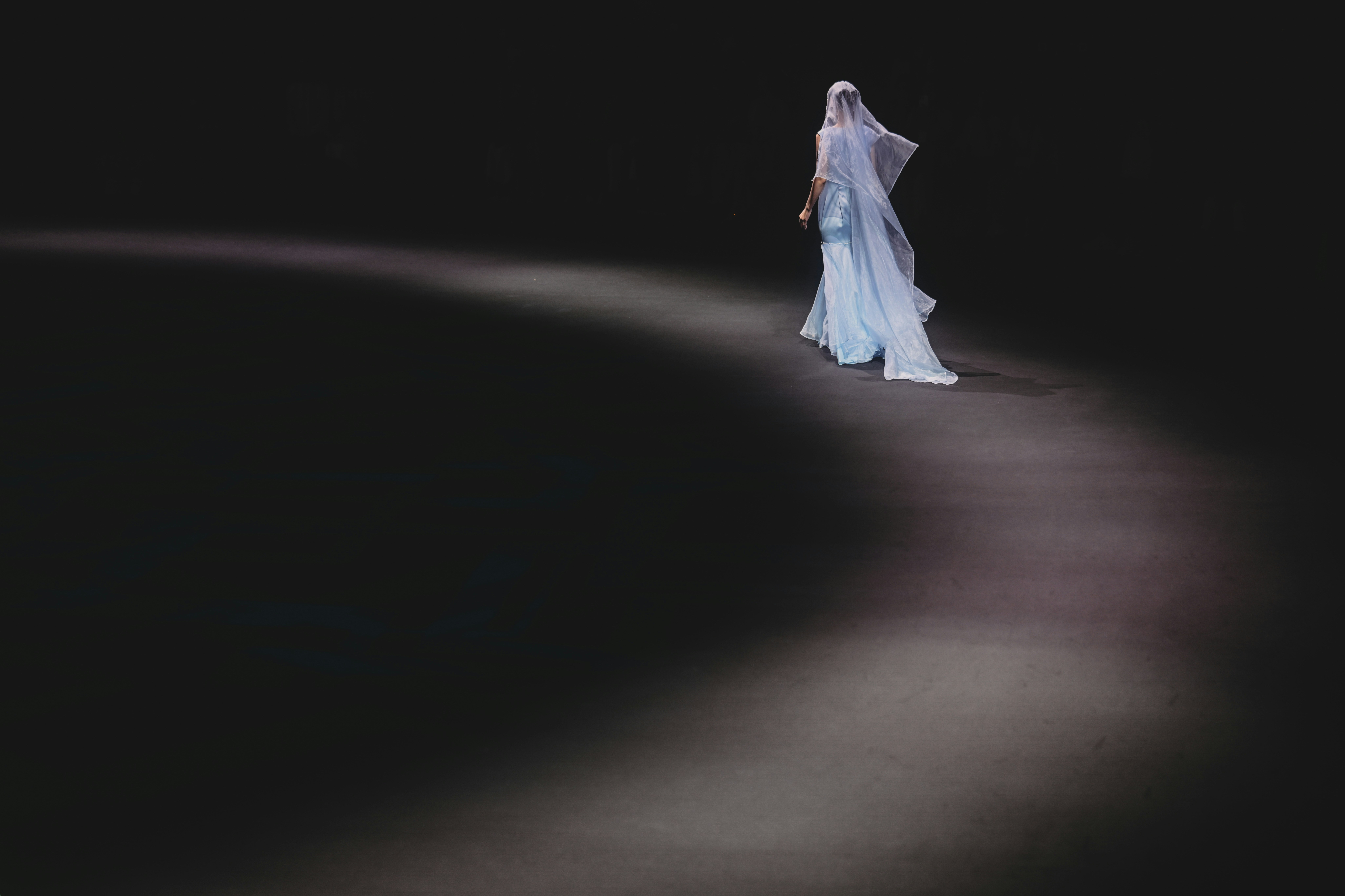 A person in a light blue gown walking on a dark runway