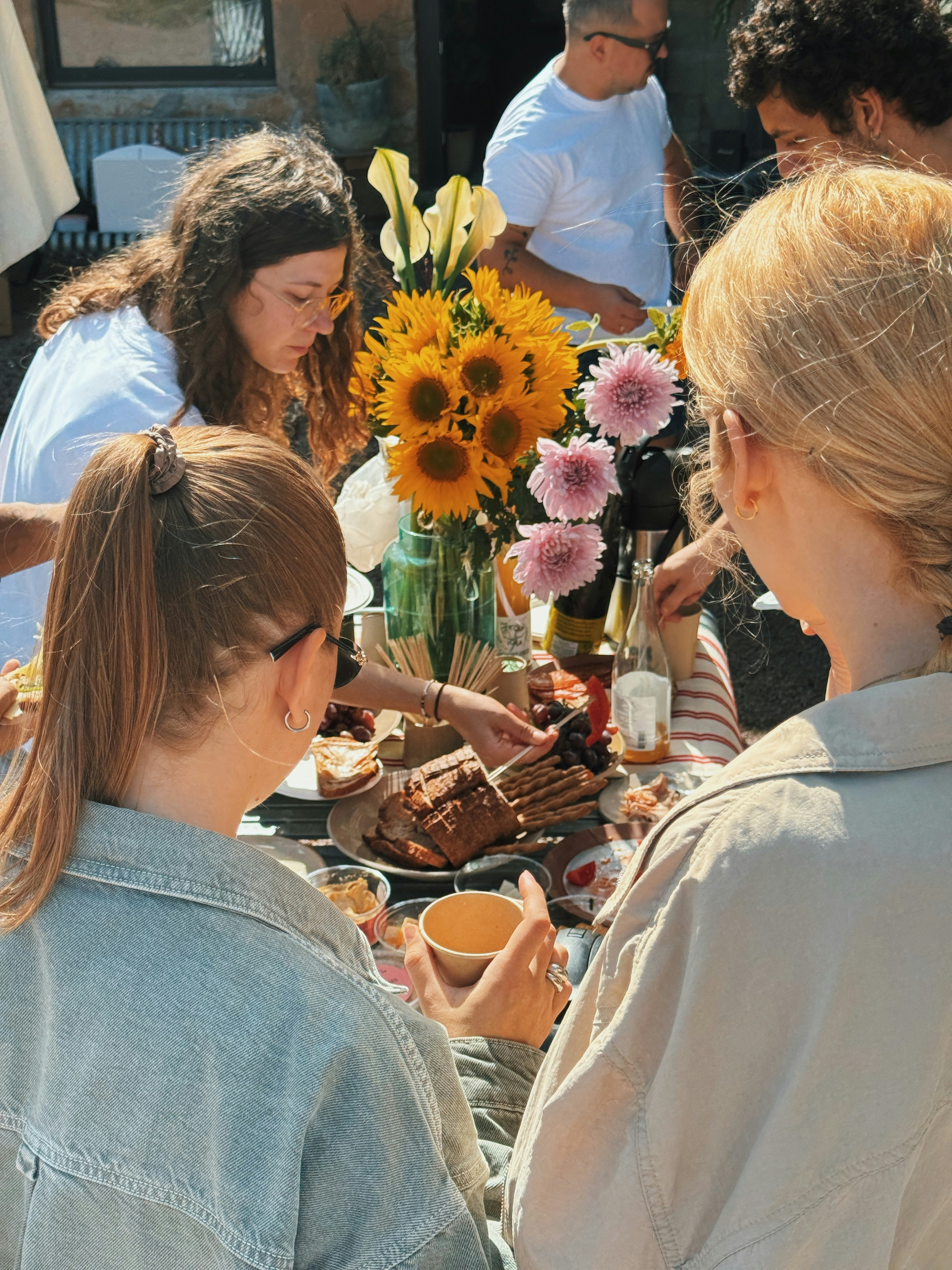 A group of people gathered around a table with flowers and food outdoors