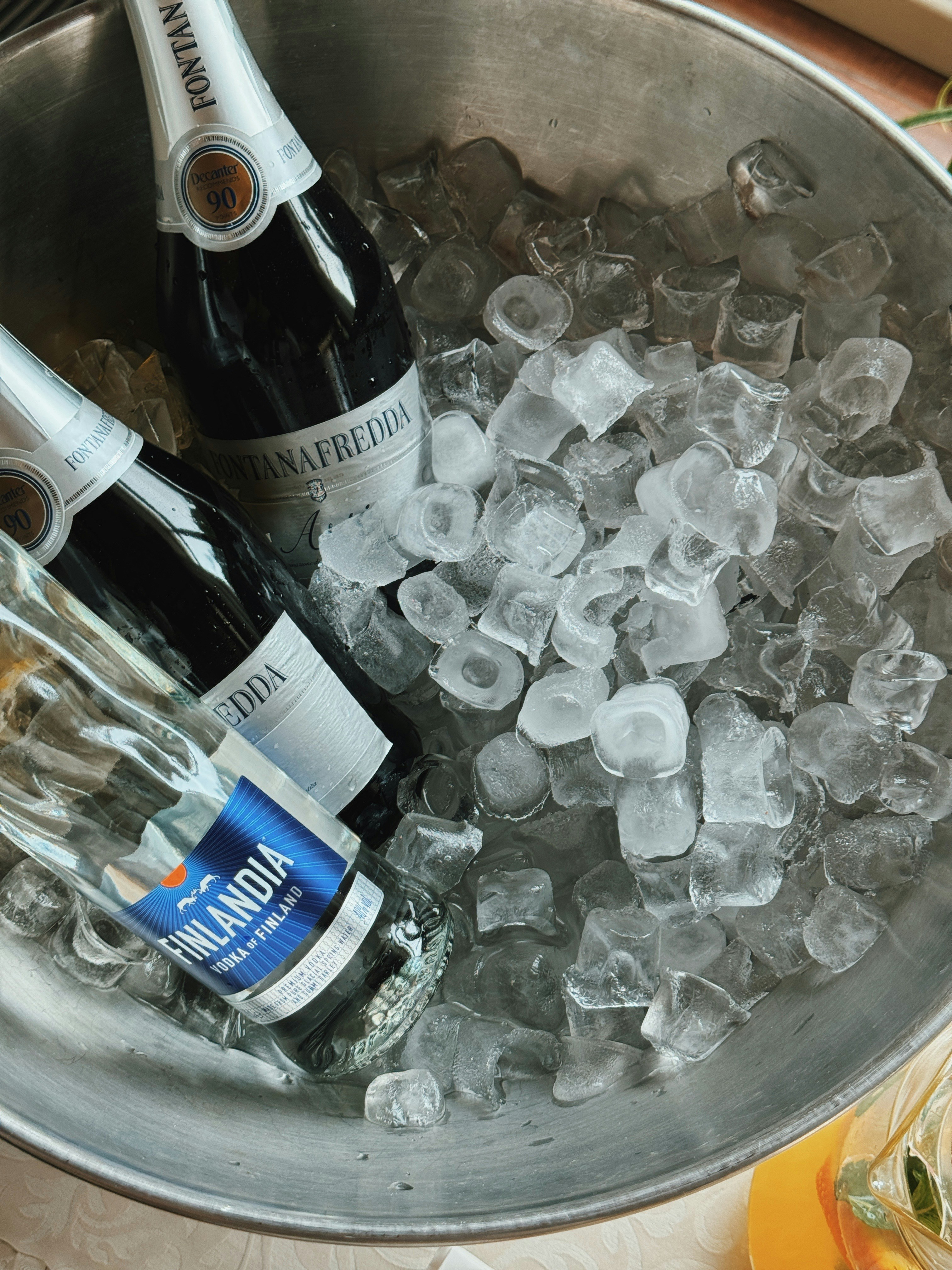 Two bottles of wine and a bottle of vodka in a metal bucket of ice