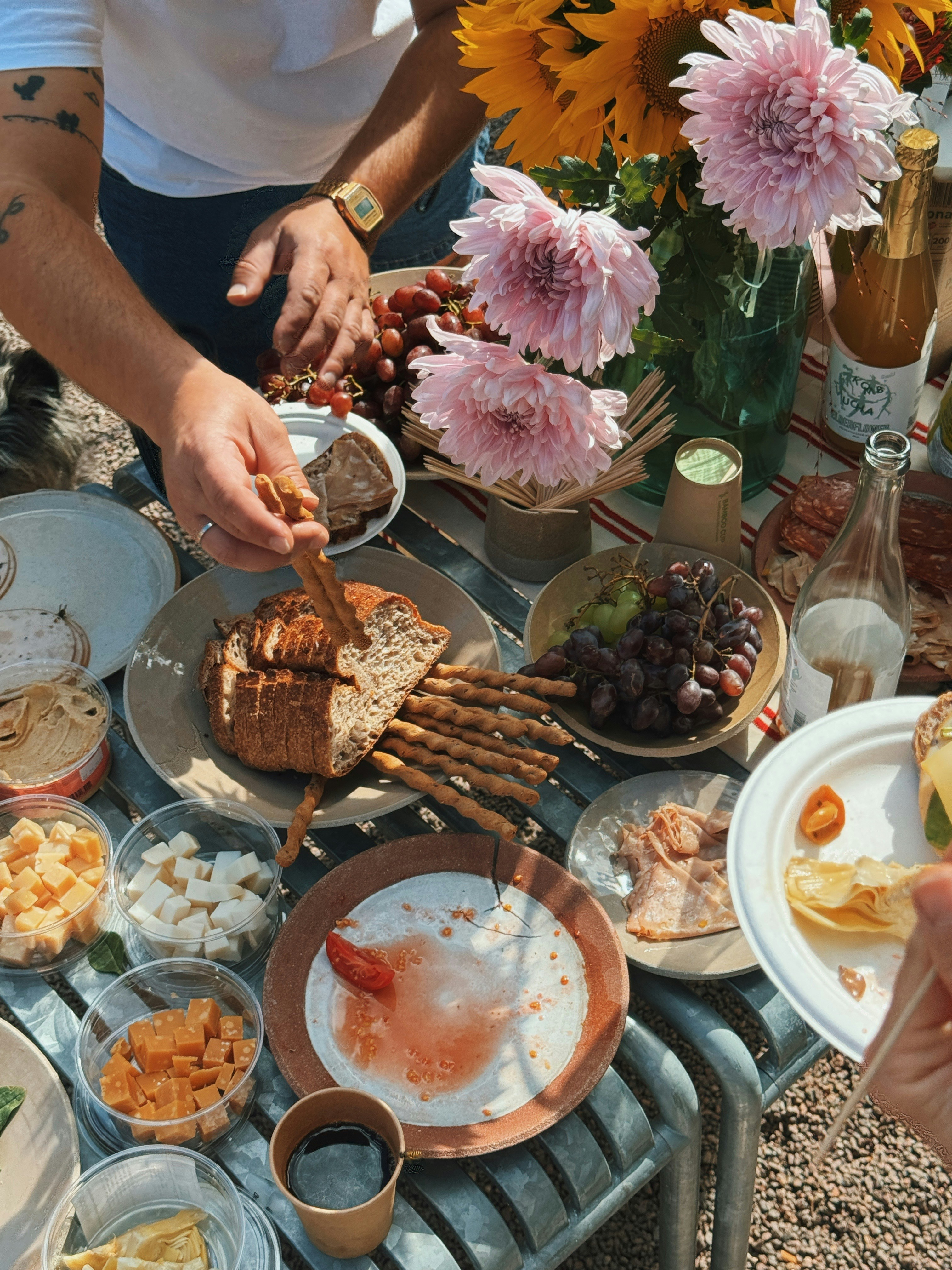 A person reaching for a breadstick on a table spread with cheese, grapes, and bread