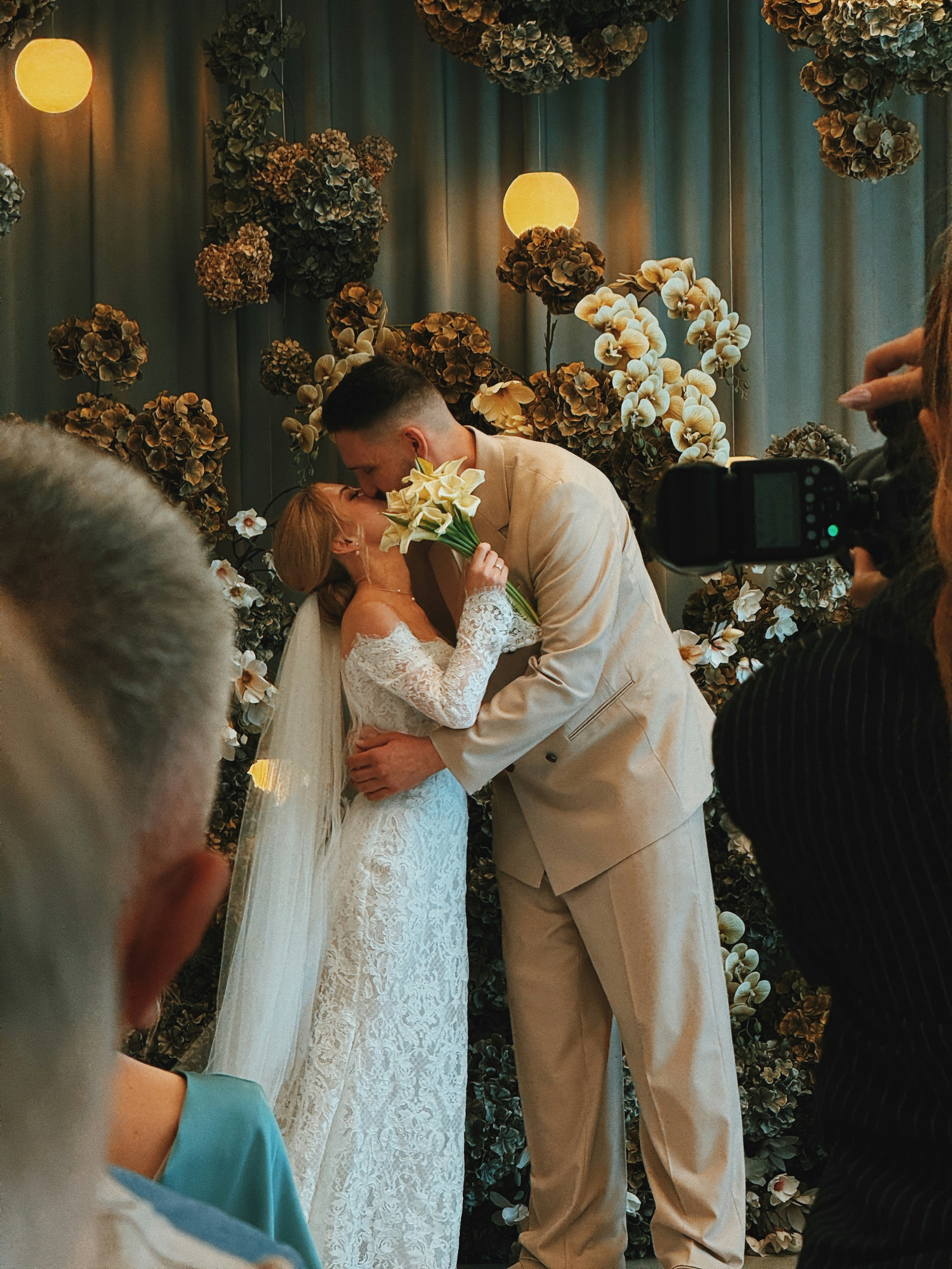 A bride and groom kissing in front of a floral wall at a wedding