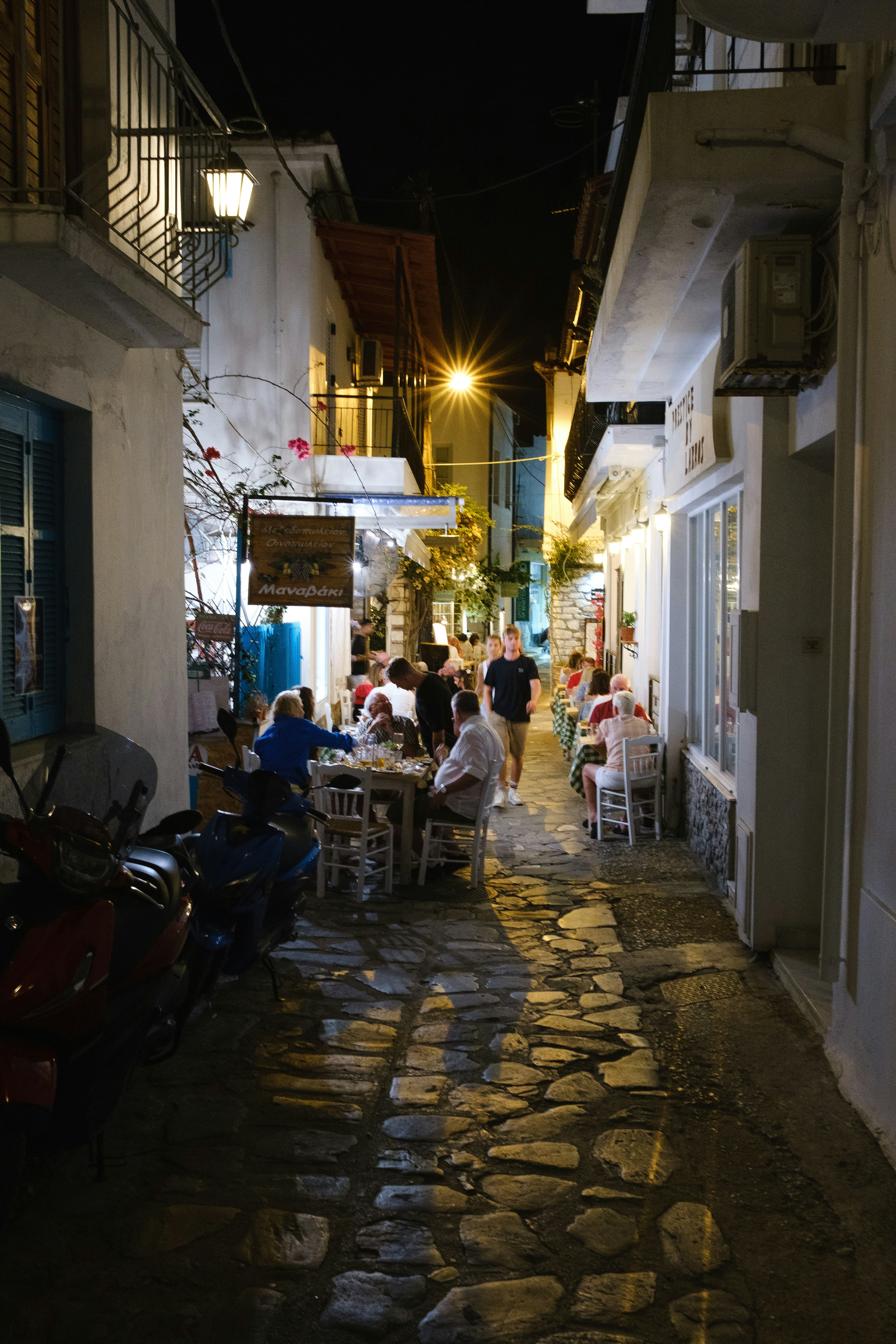 Abends essen Menschen an Tischen in einer engen Kopfsteinpflastergasse