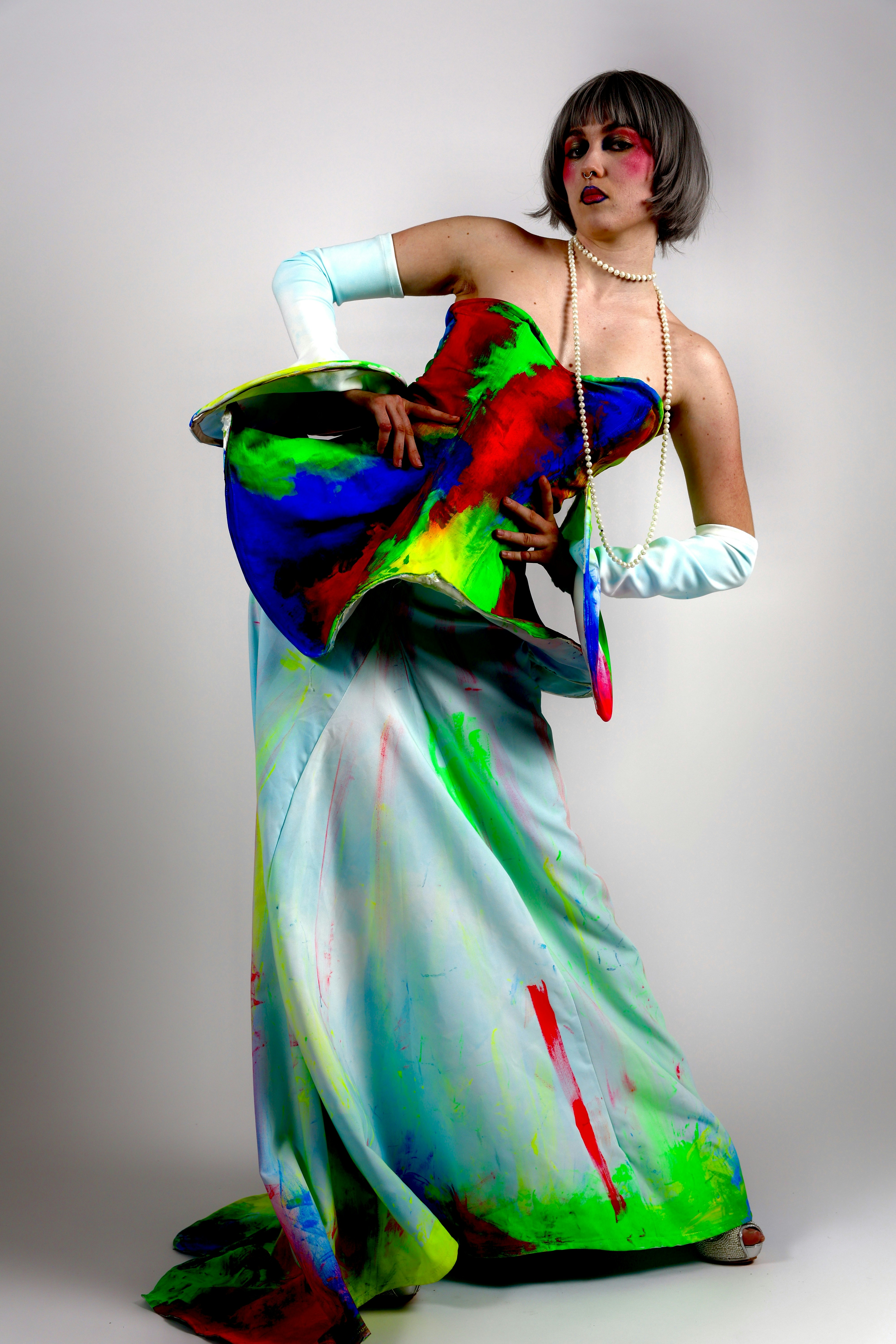 A person in a paint-splattered gown and long gloves with a pearl necklace