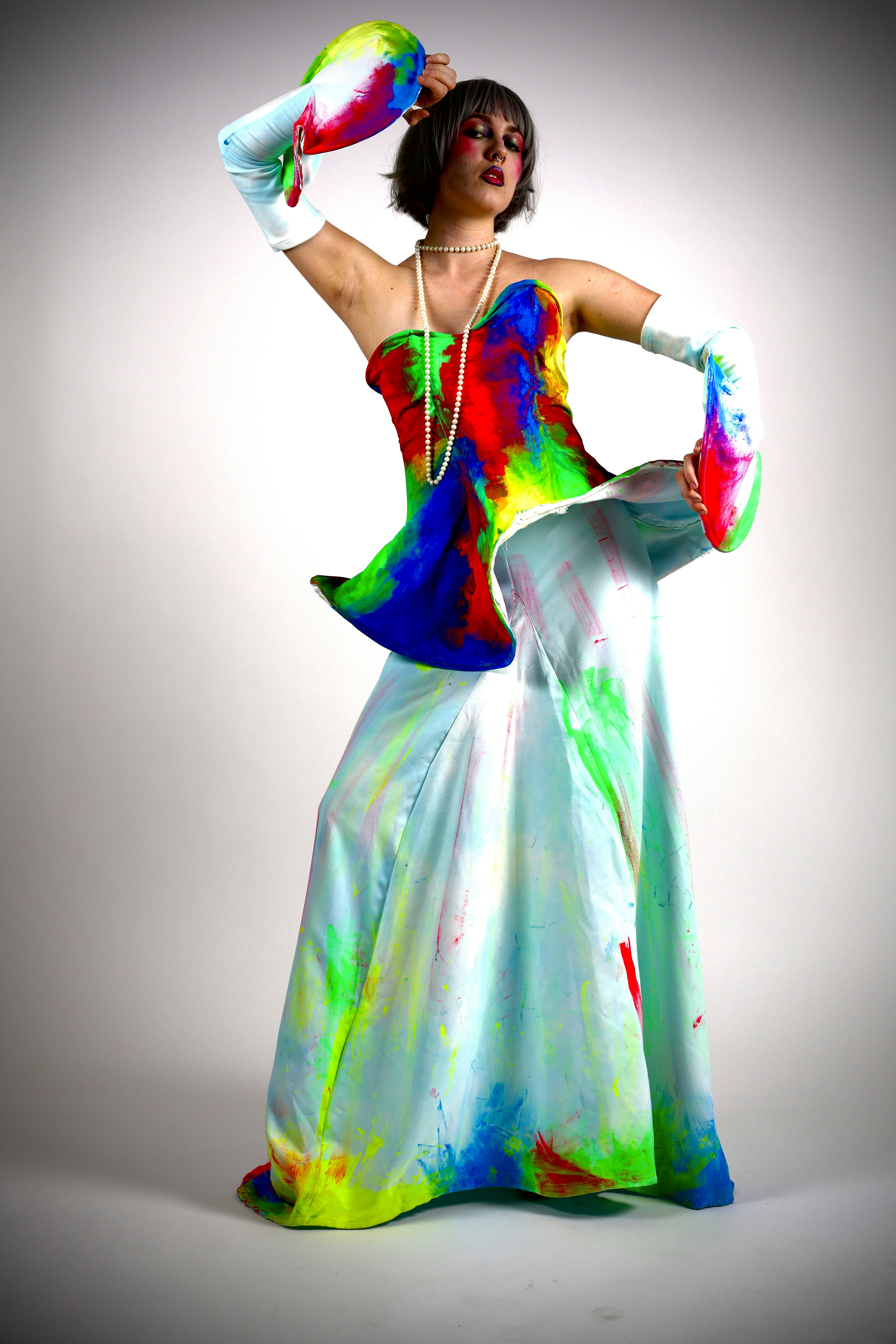 A person wearing a paint-splattered gown and gloves with a pearl necklace