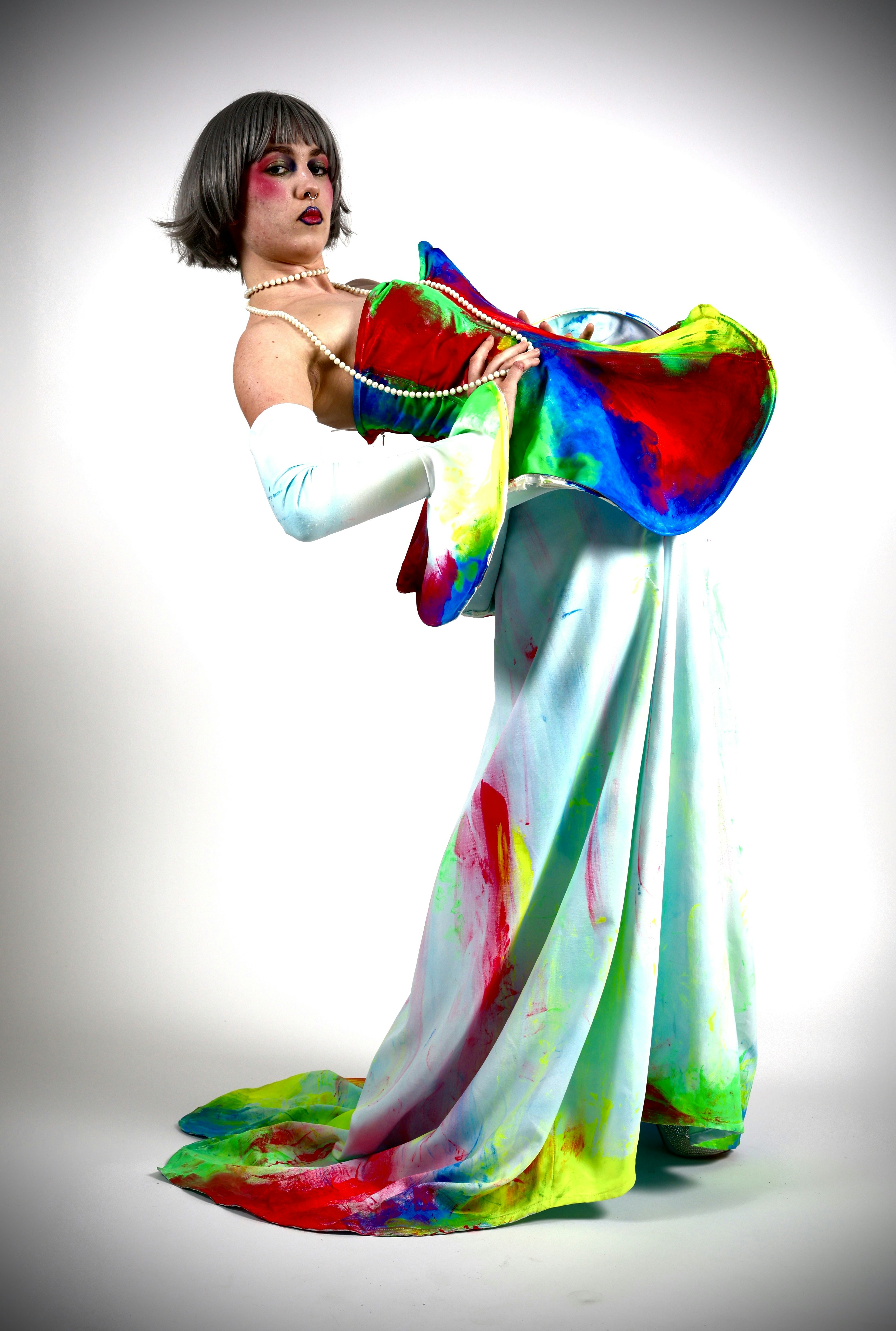 A person in a paint-splattered gown and white gloves wearing a pearl necklace