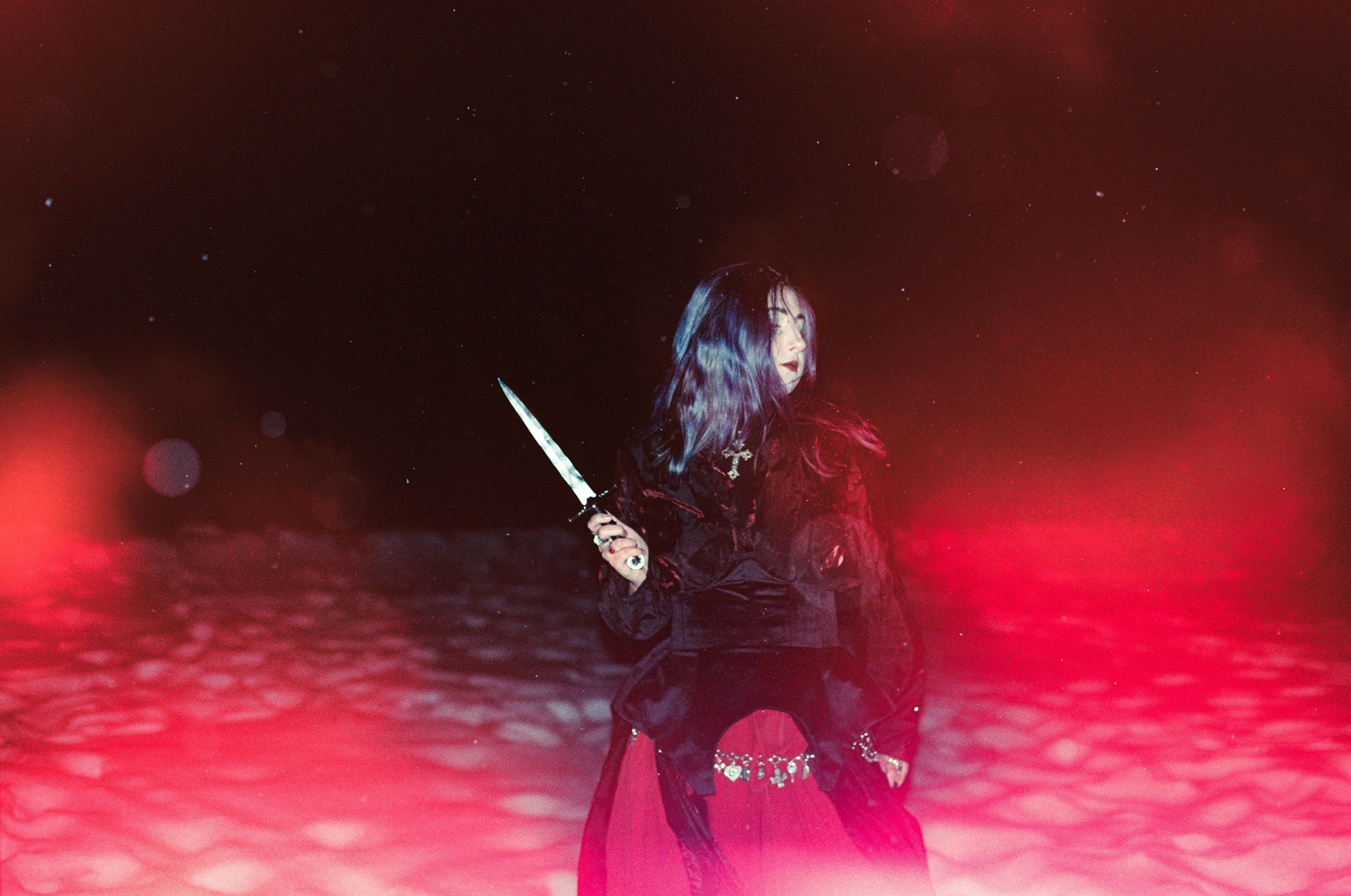 A person with dark hair holding a dagger in a red-lit environment