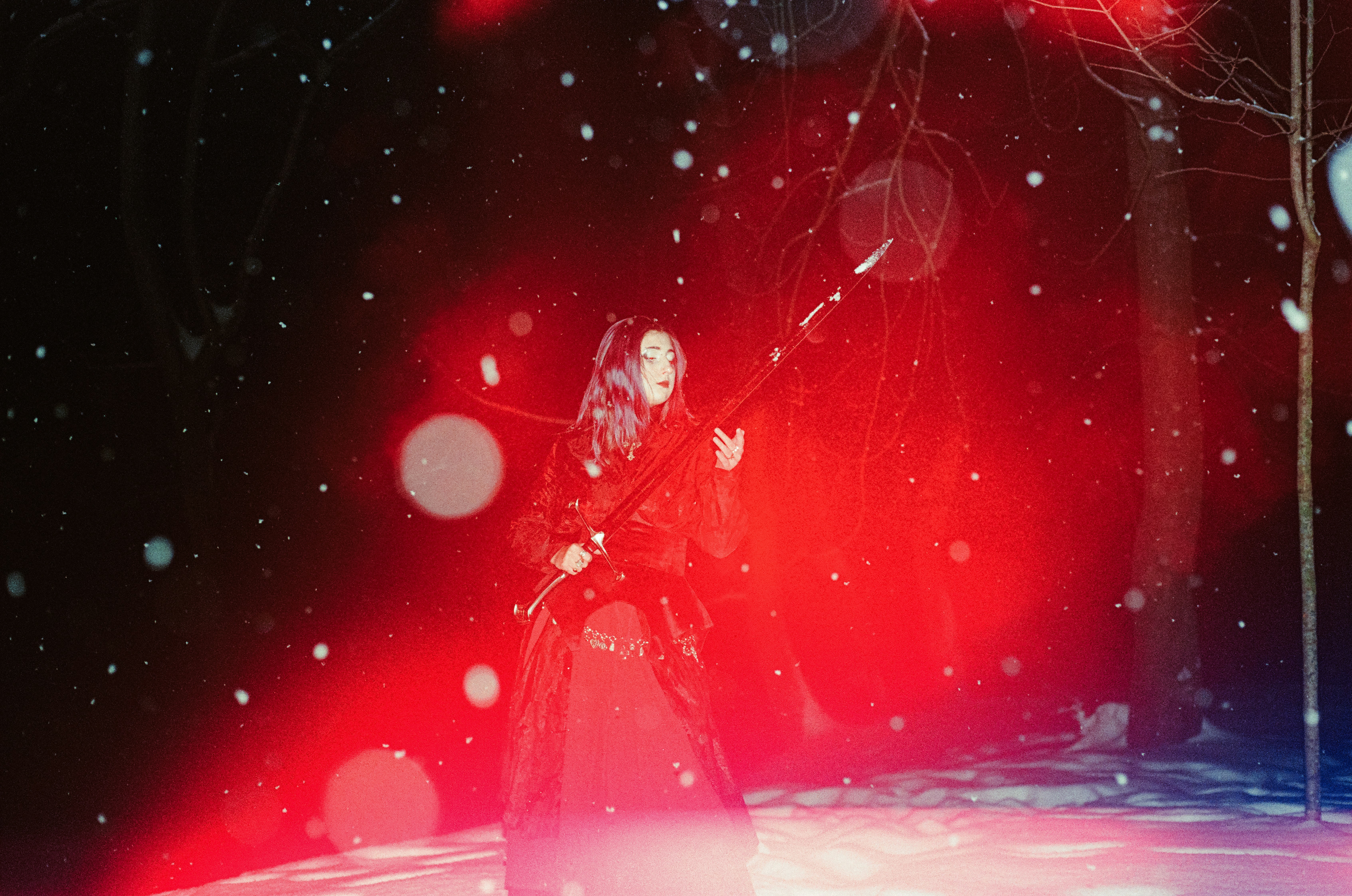 A person in a dark dress holding a sword in a snowy forest
