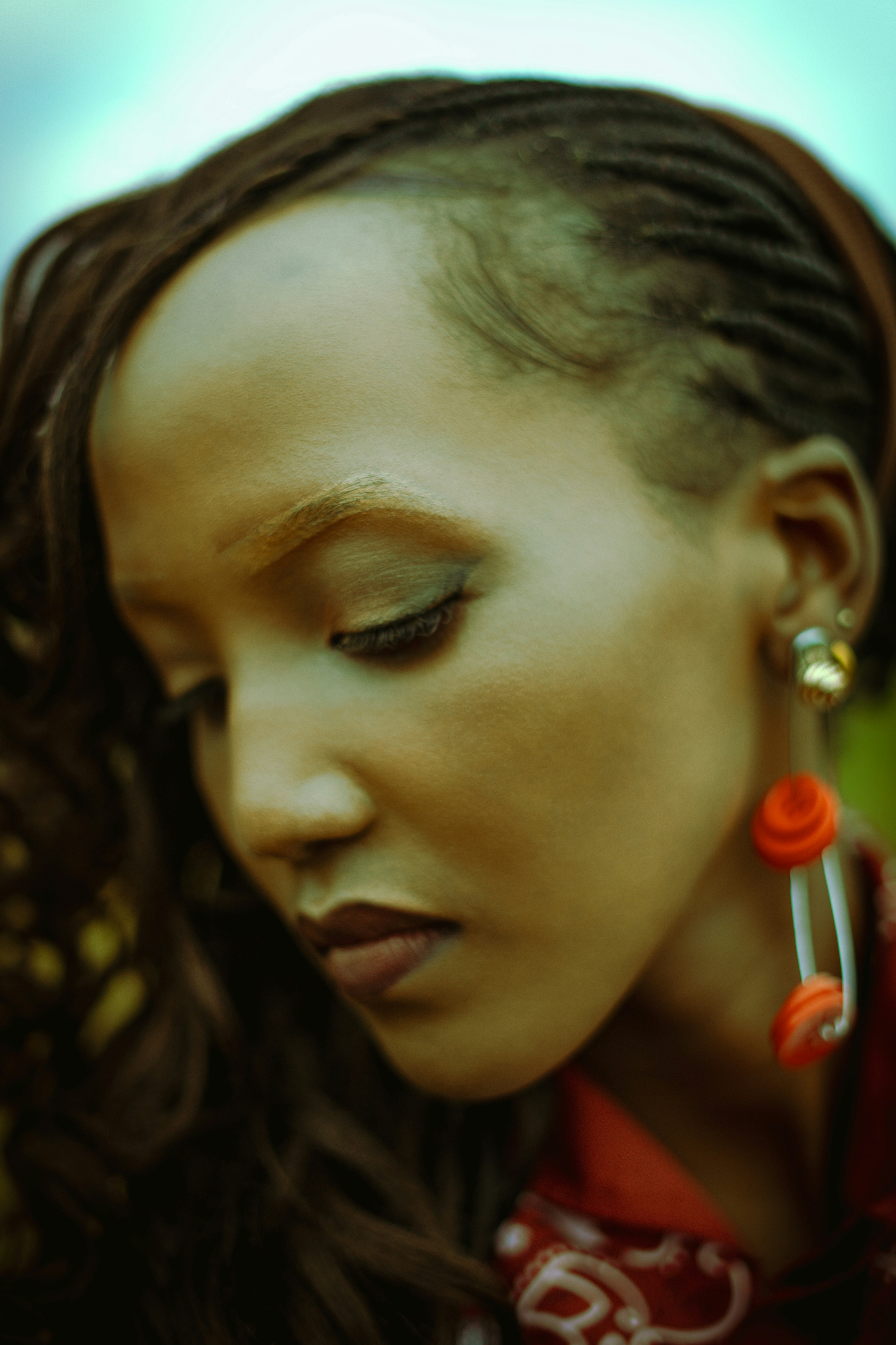 A woman with braided hair wearing long orange button earrings in profile
