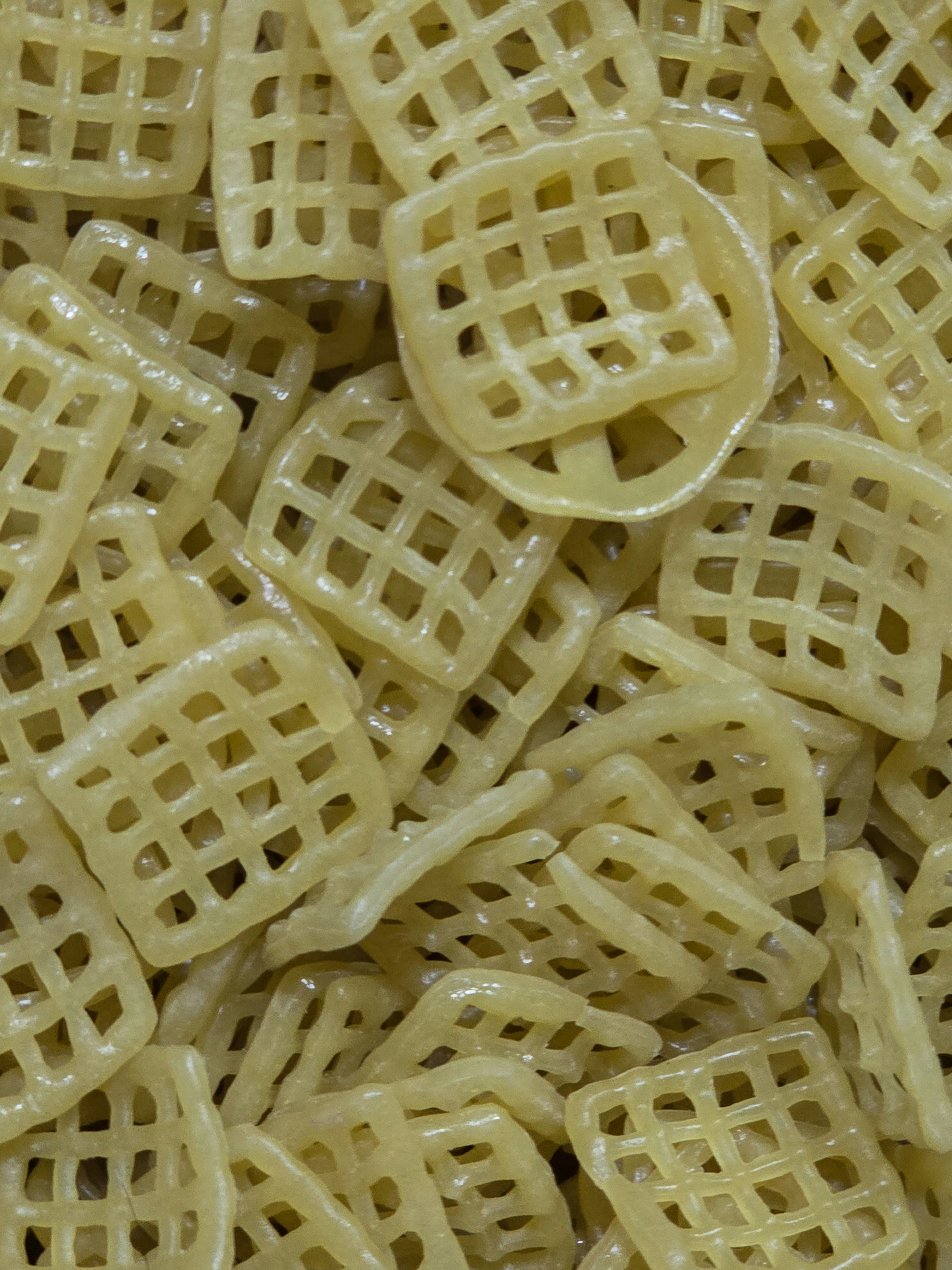 A pile of small square grid shaped dried pasta snacks