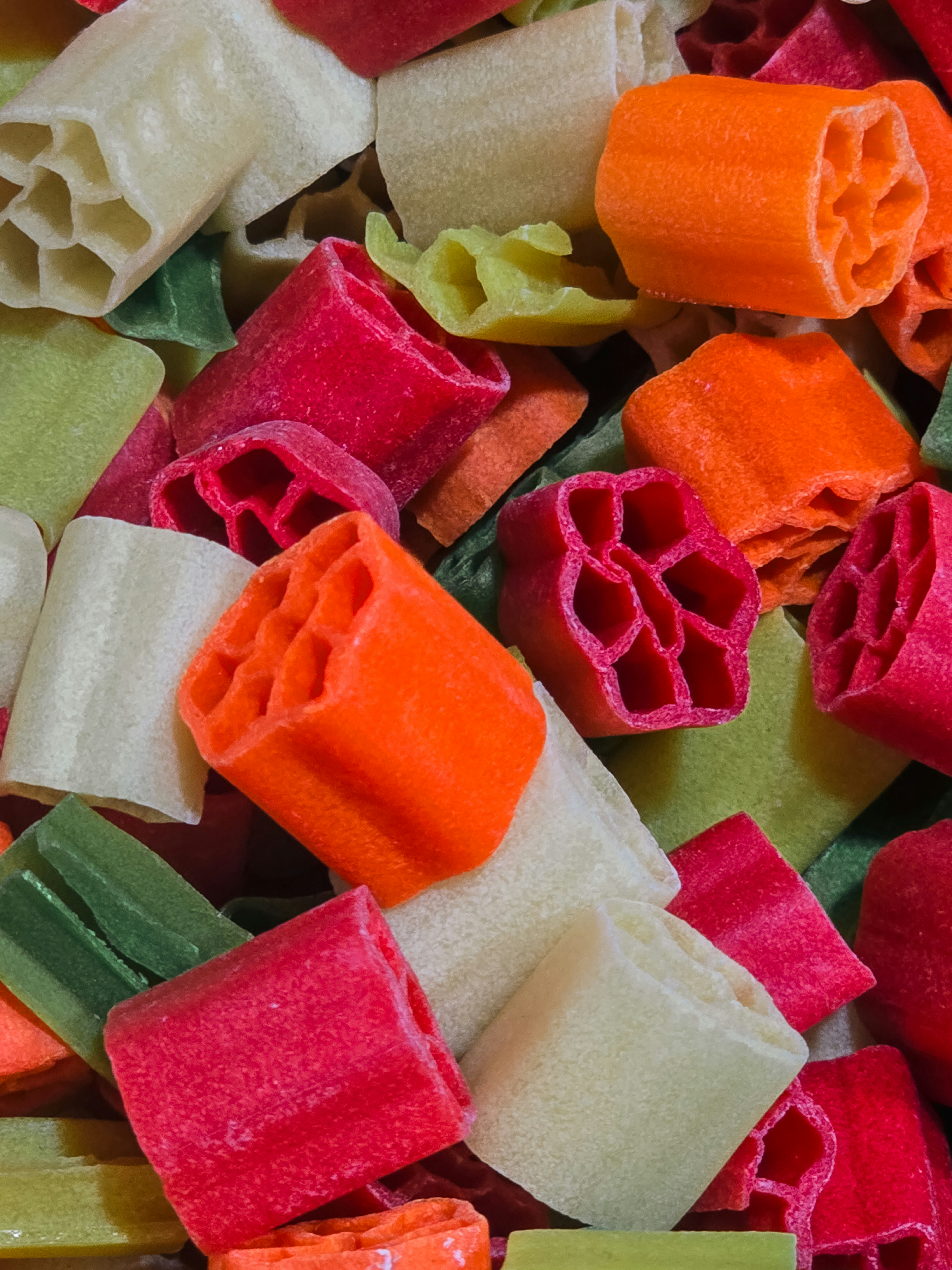 A pile of colorful wagon wheel shaped pasta in red, orange, green, and white