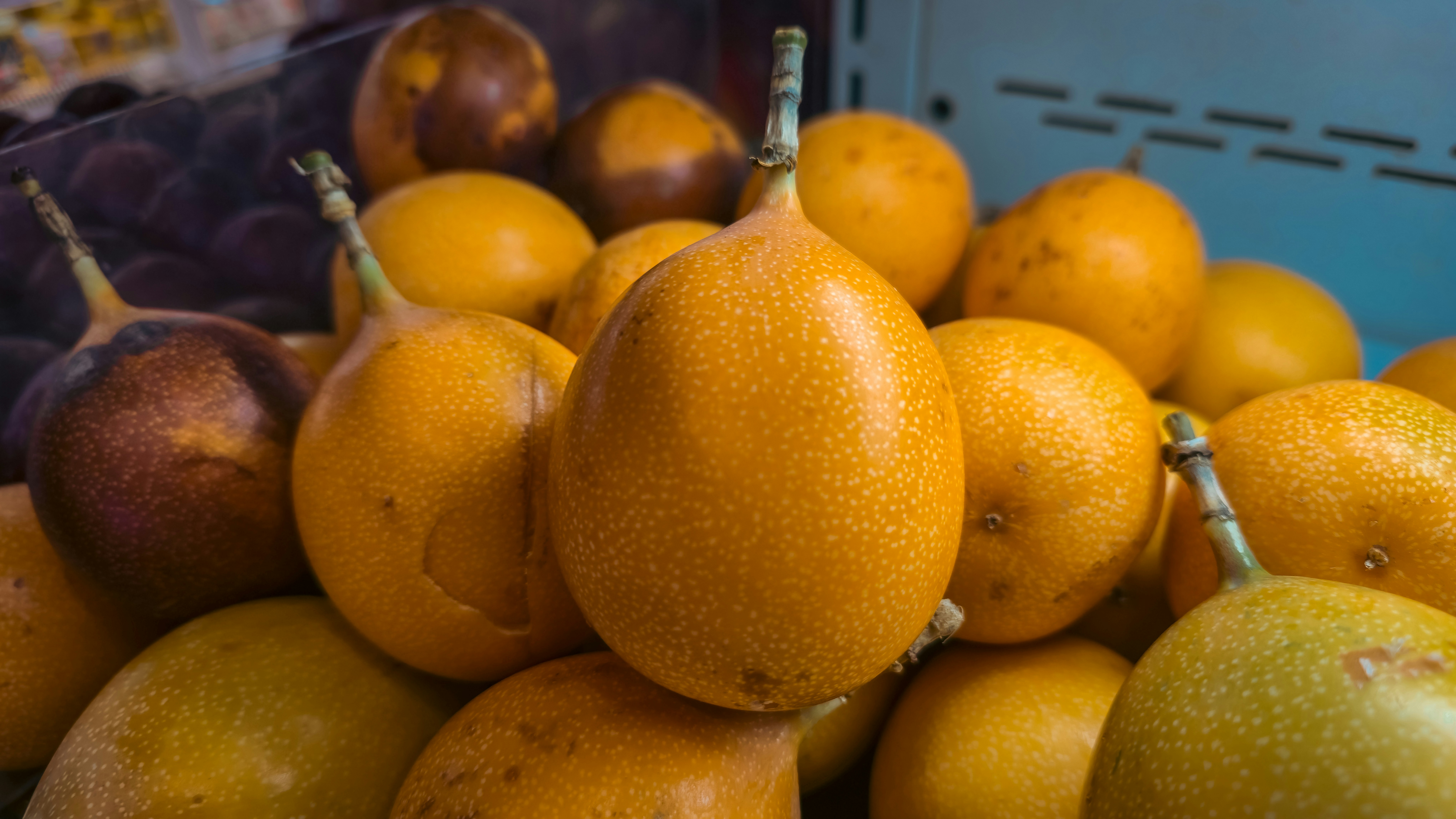 A pile of yellow granadilla fruits with speckled skins in a market bin