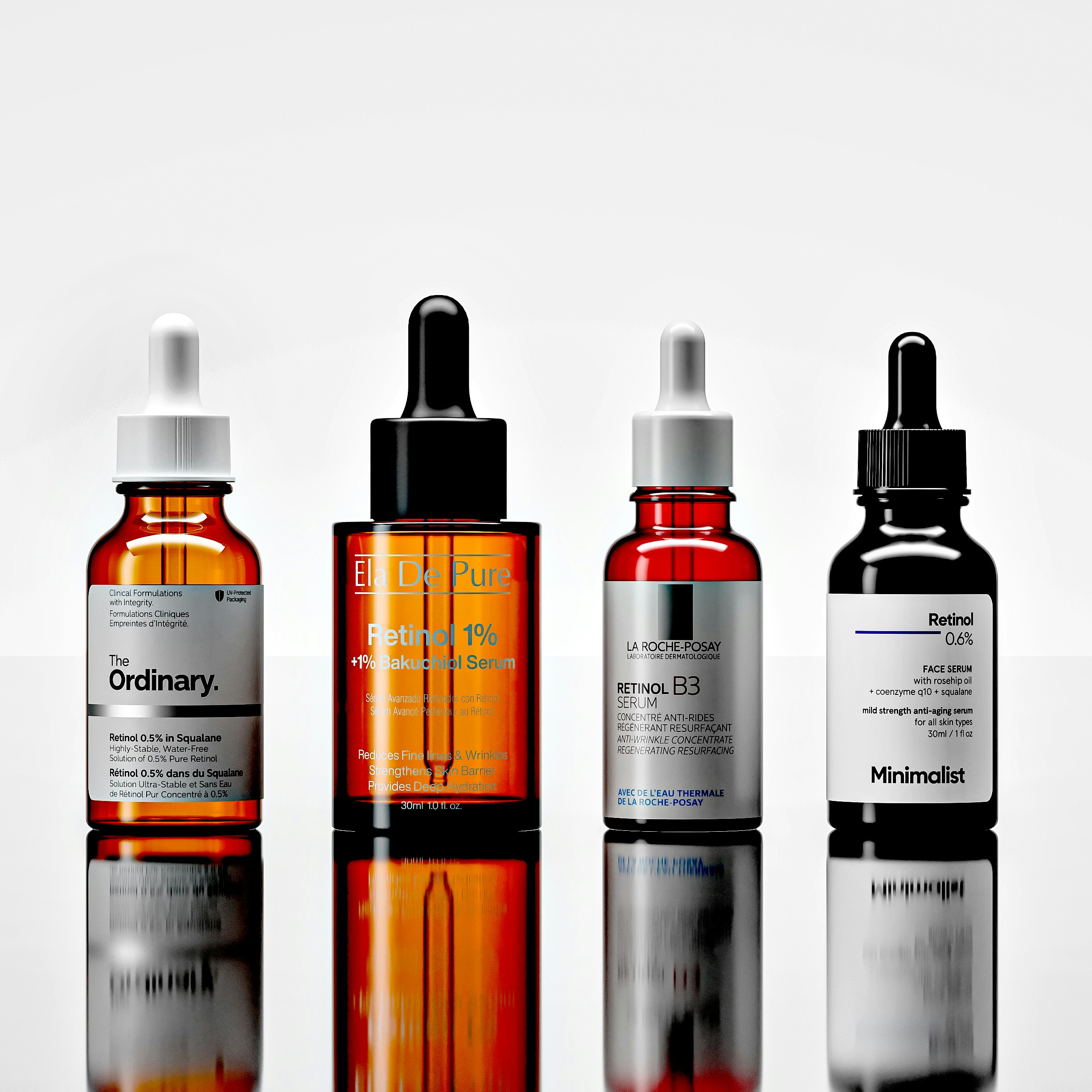 Four glass dropper bottles of facial serum standing on a reflective white surface