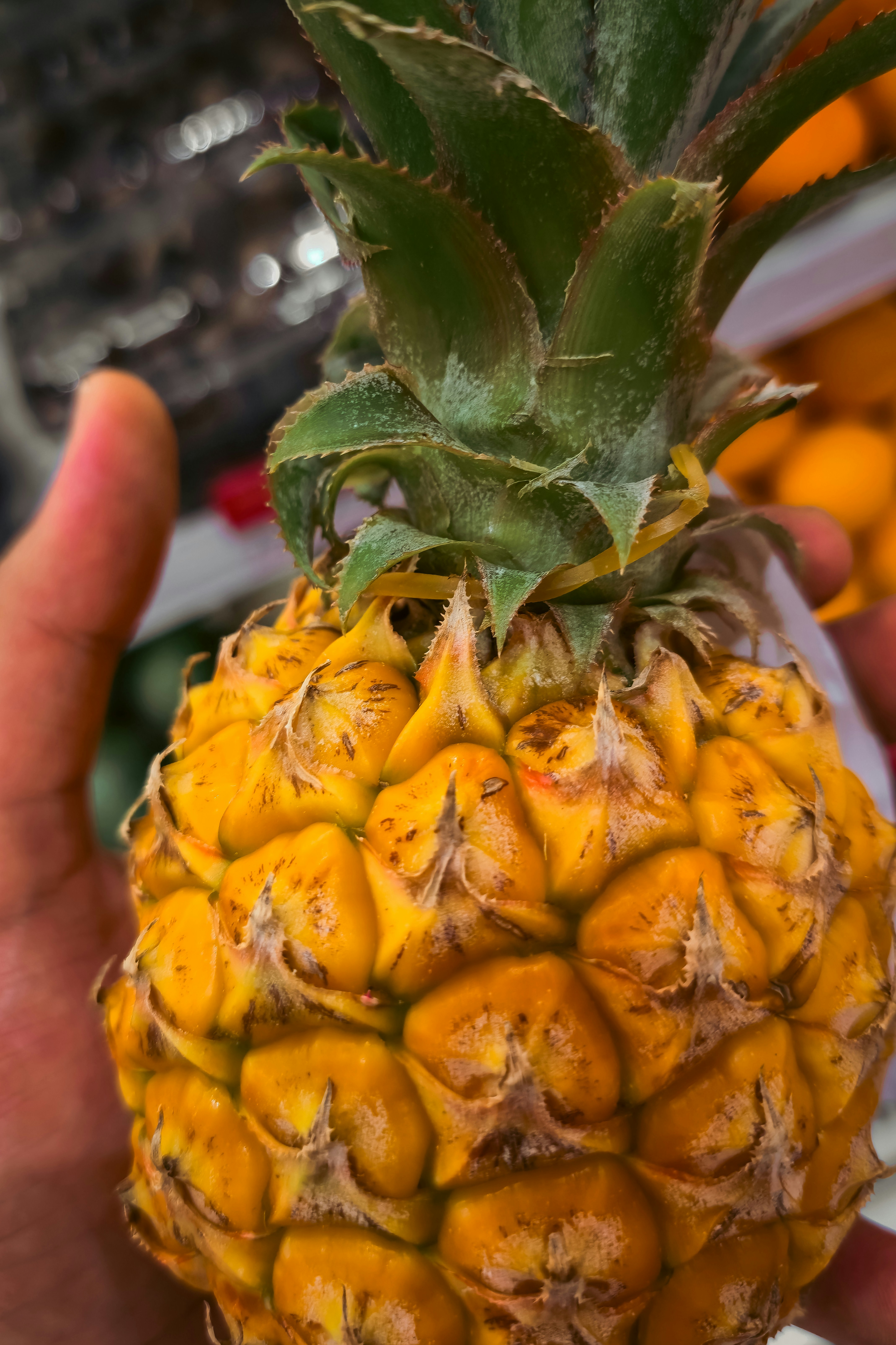 A hand holding a ripe yellow pineapple with green leaves in a store
