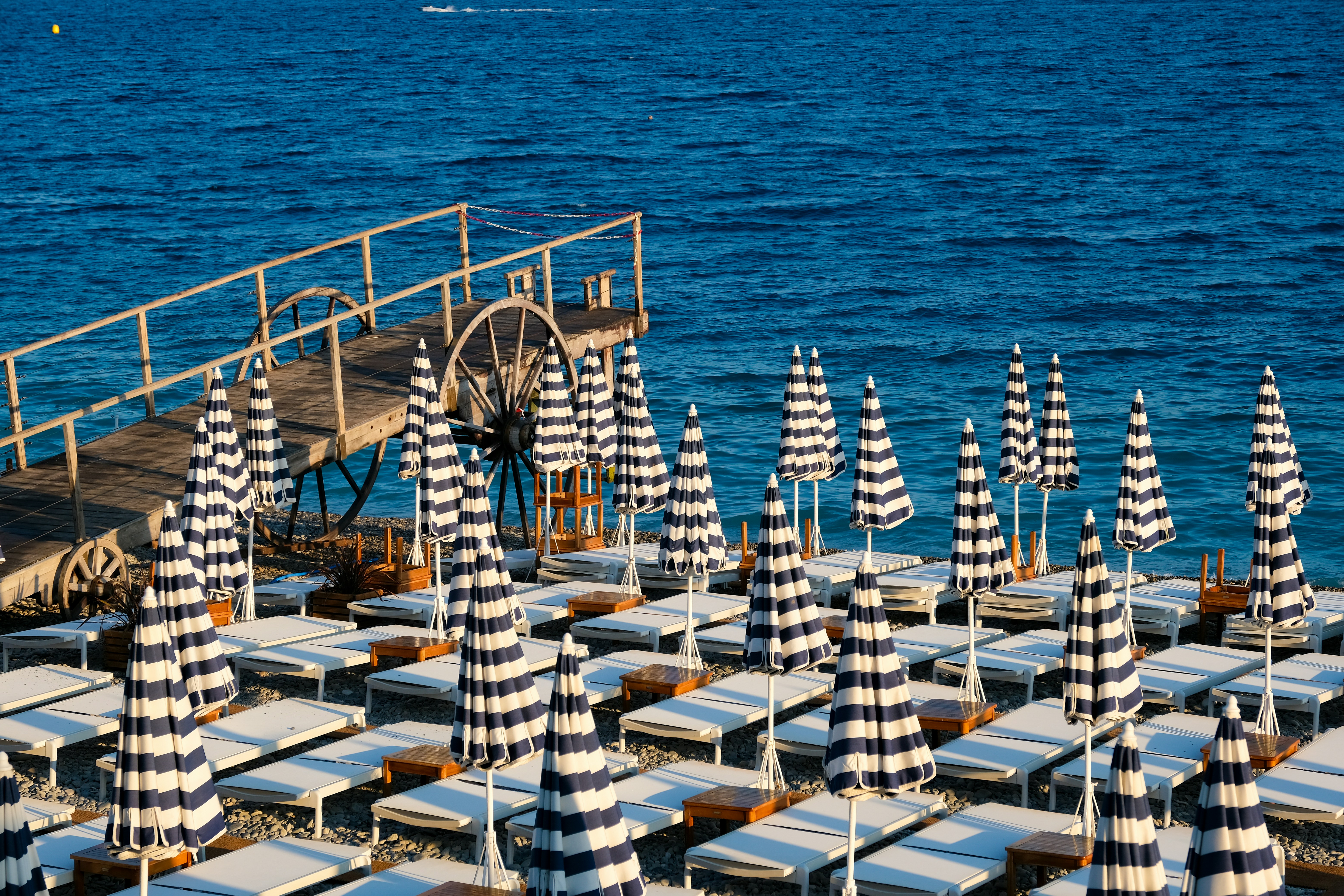 Blue and white striped beach umbrellas over lounge chairs on a pebble beach