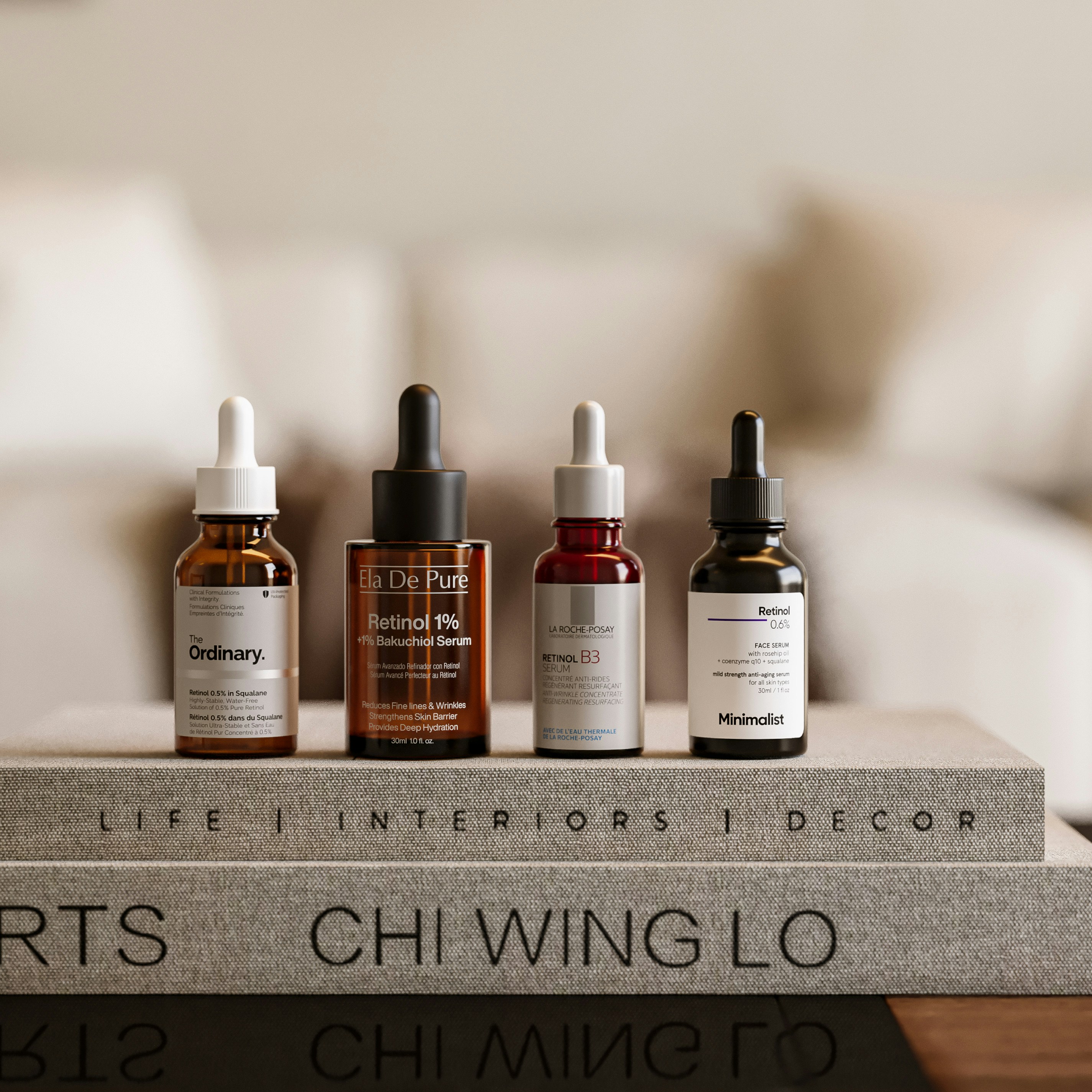 Four glass dropper bottles of skincare serum arranged on two stacked fabric books