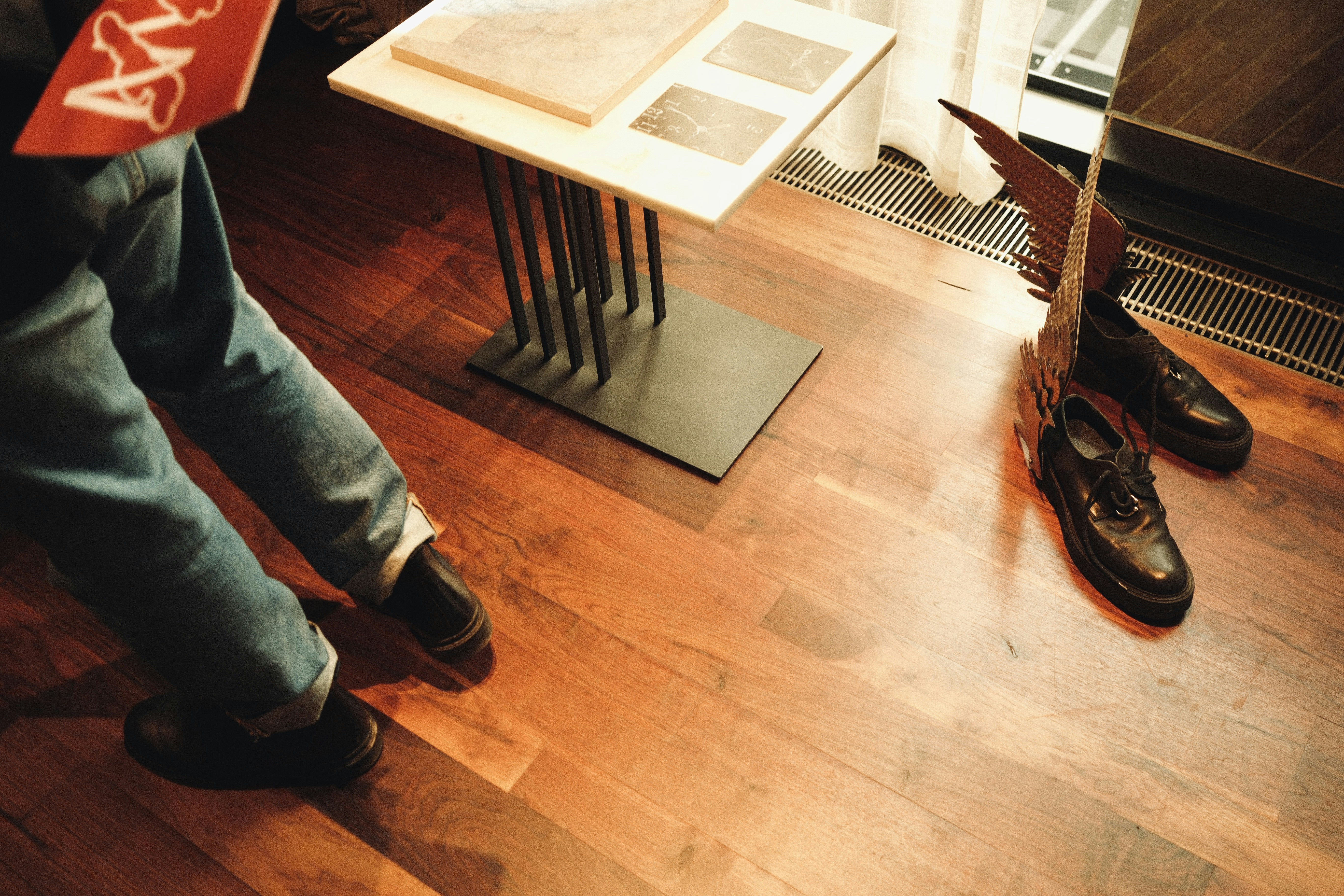 A person in jeans standing near a table and winged black shoes