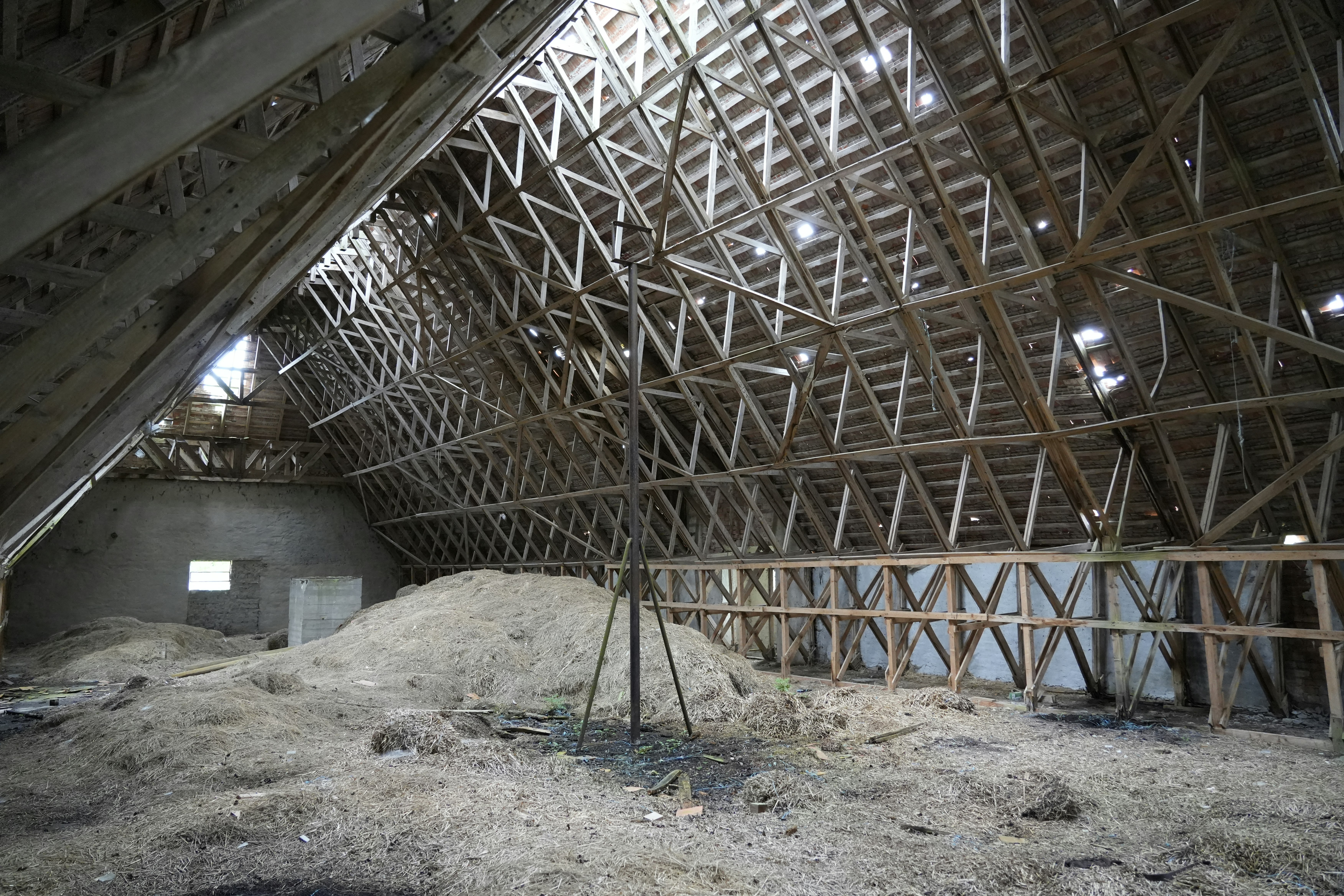 A large wooden attic with exposed roof trusses and piles of dry hay