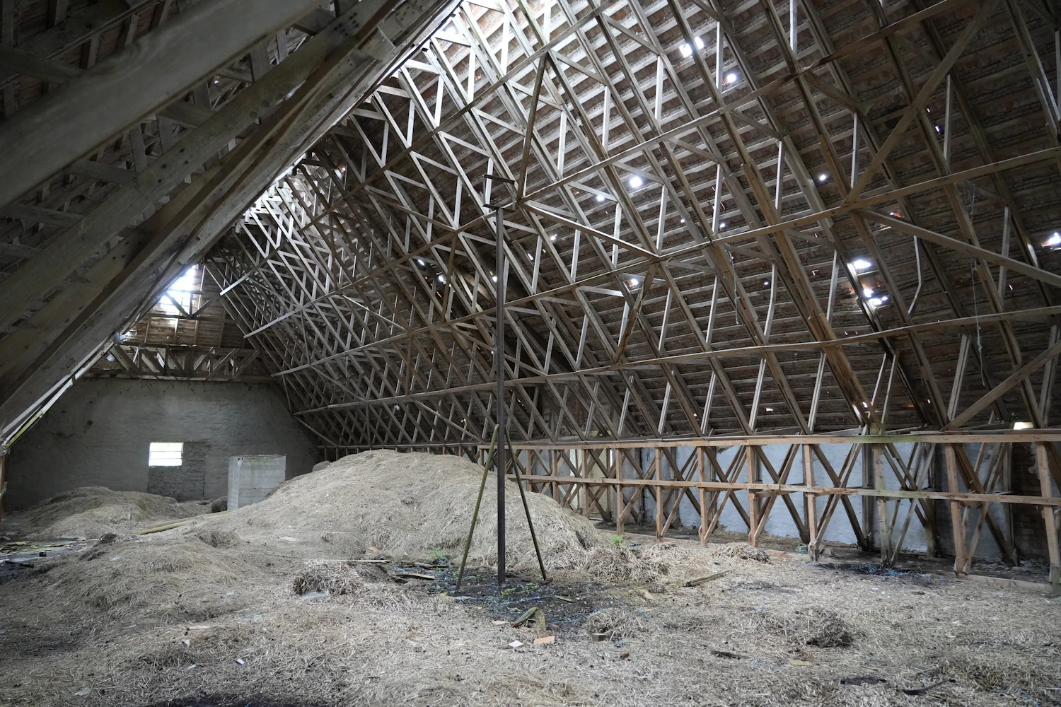 A wide timber roof structure above a heap of pale loose material in a barn