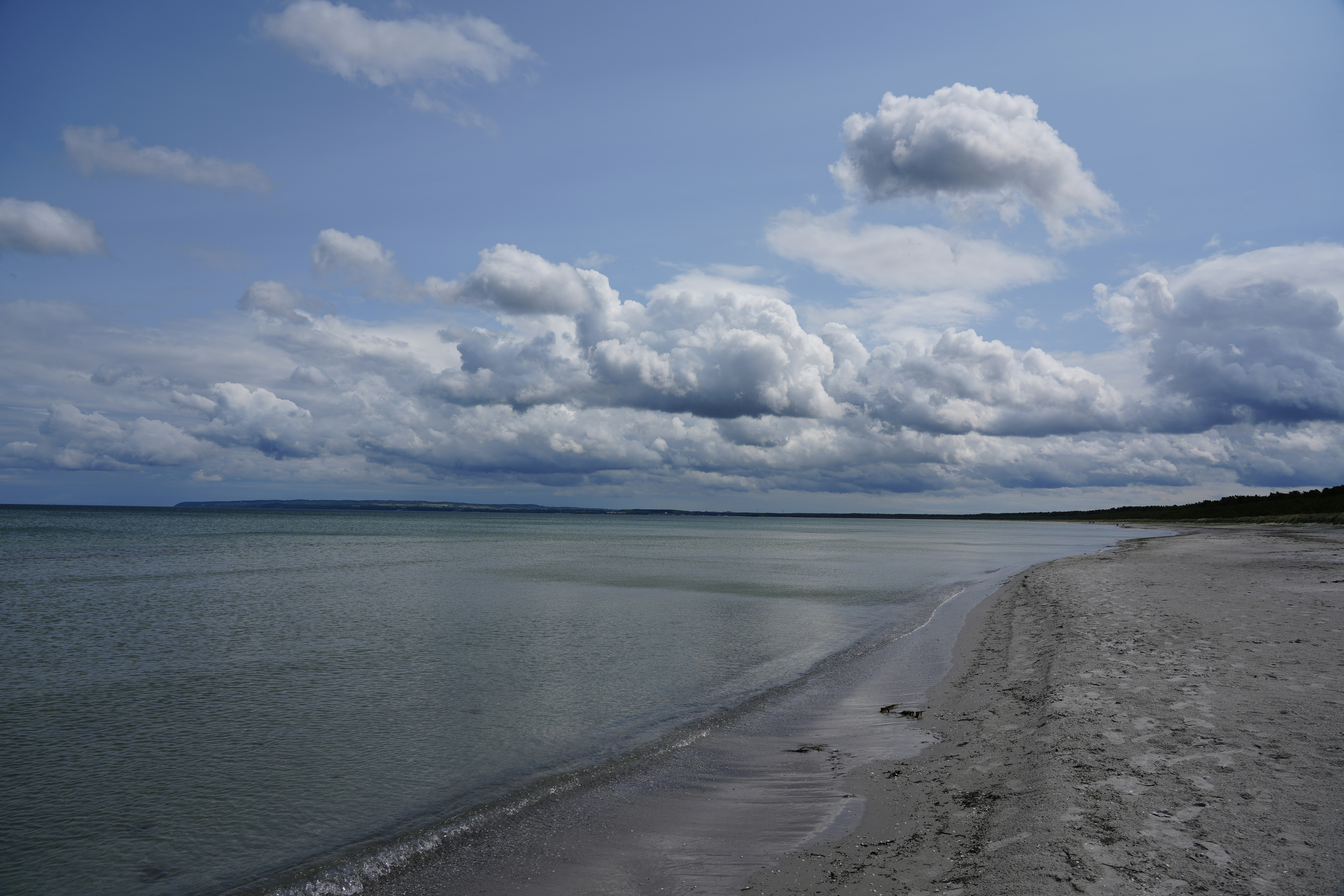 A sandy beach along a calm sea under a sky with scattered clouds