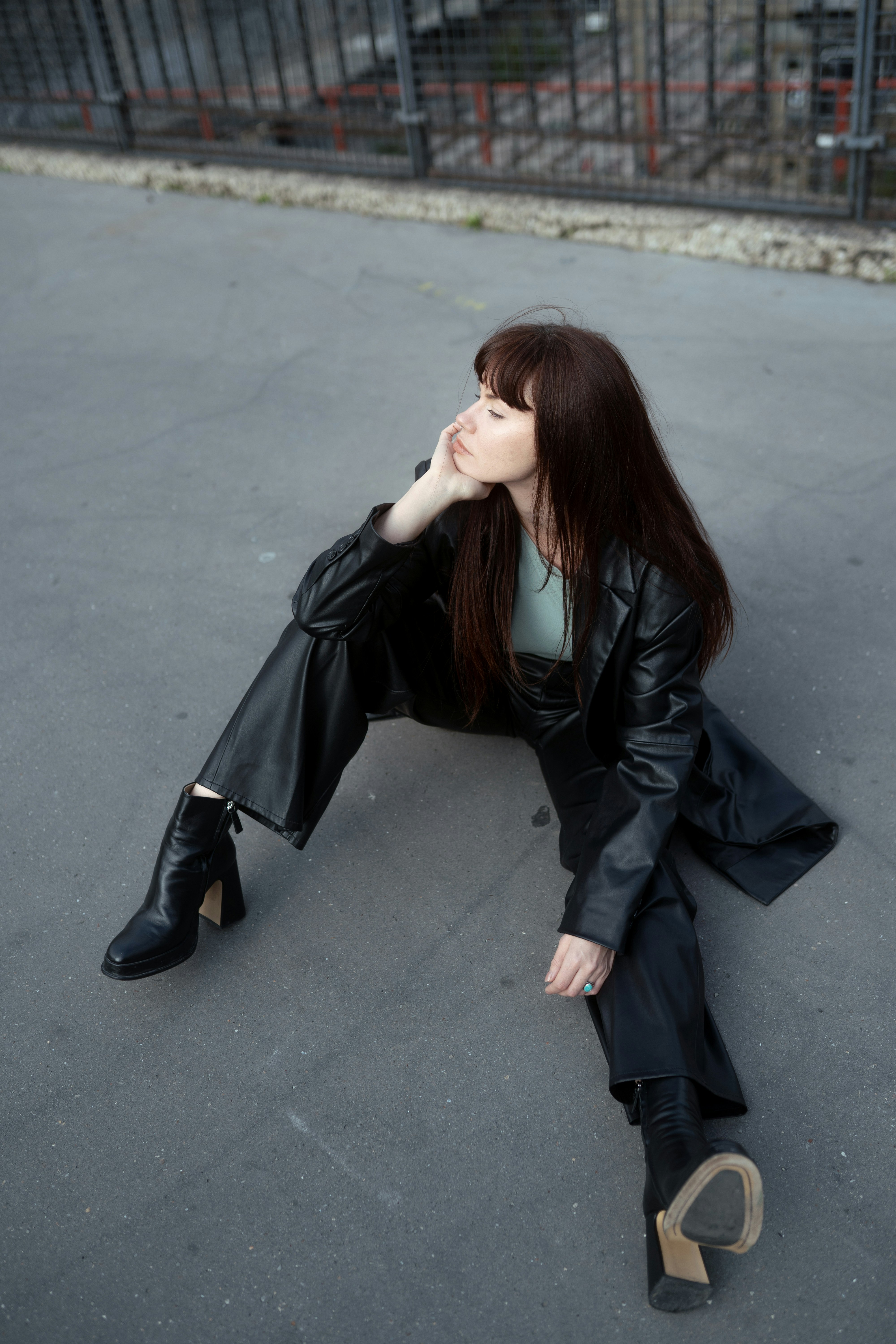A woman in a black leather suit sitting on grey pavement