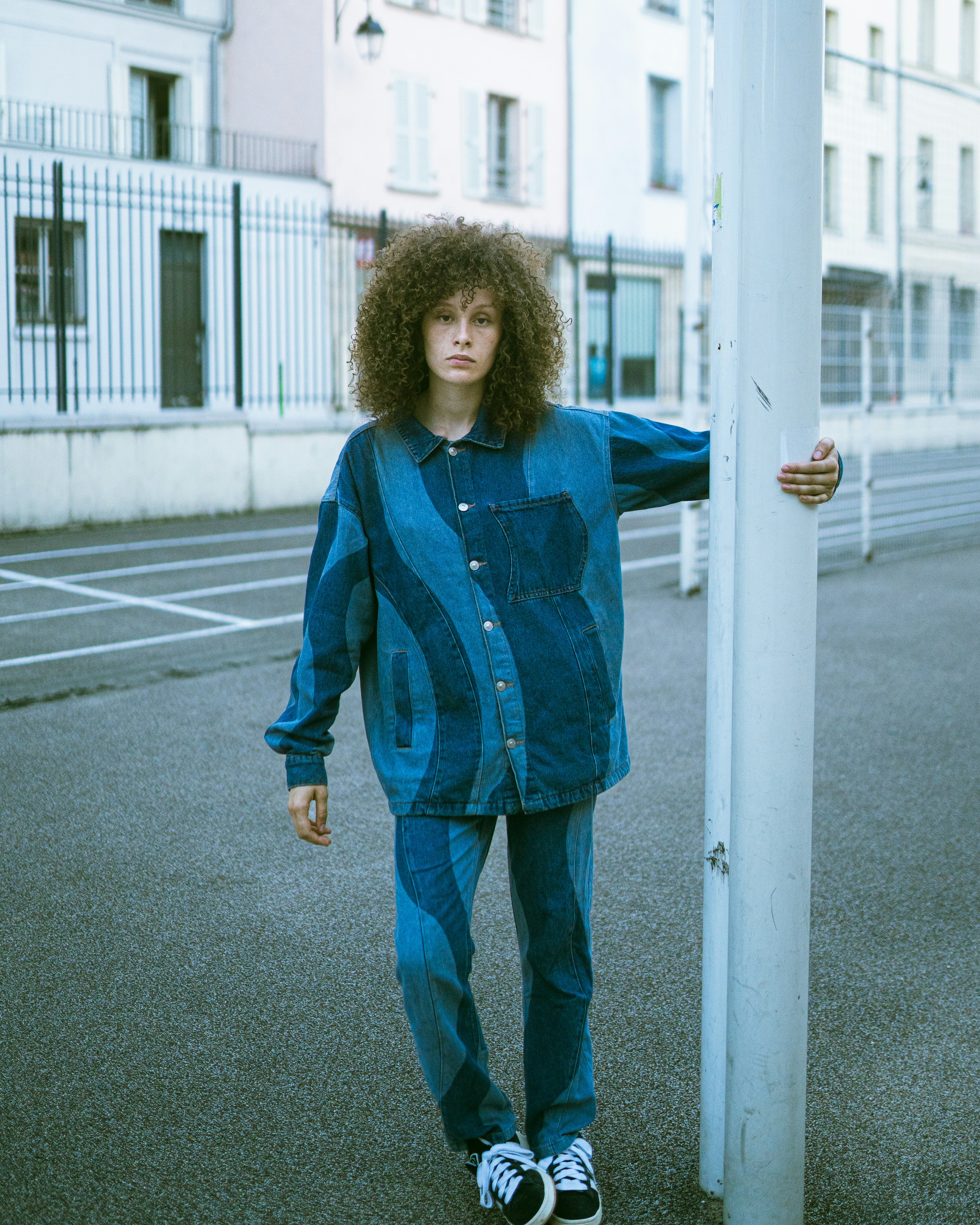 A person with curly hair wearing a patchwork denim outfit on a city street