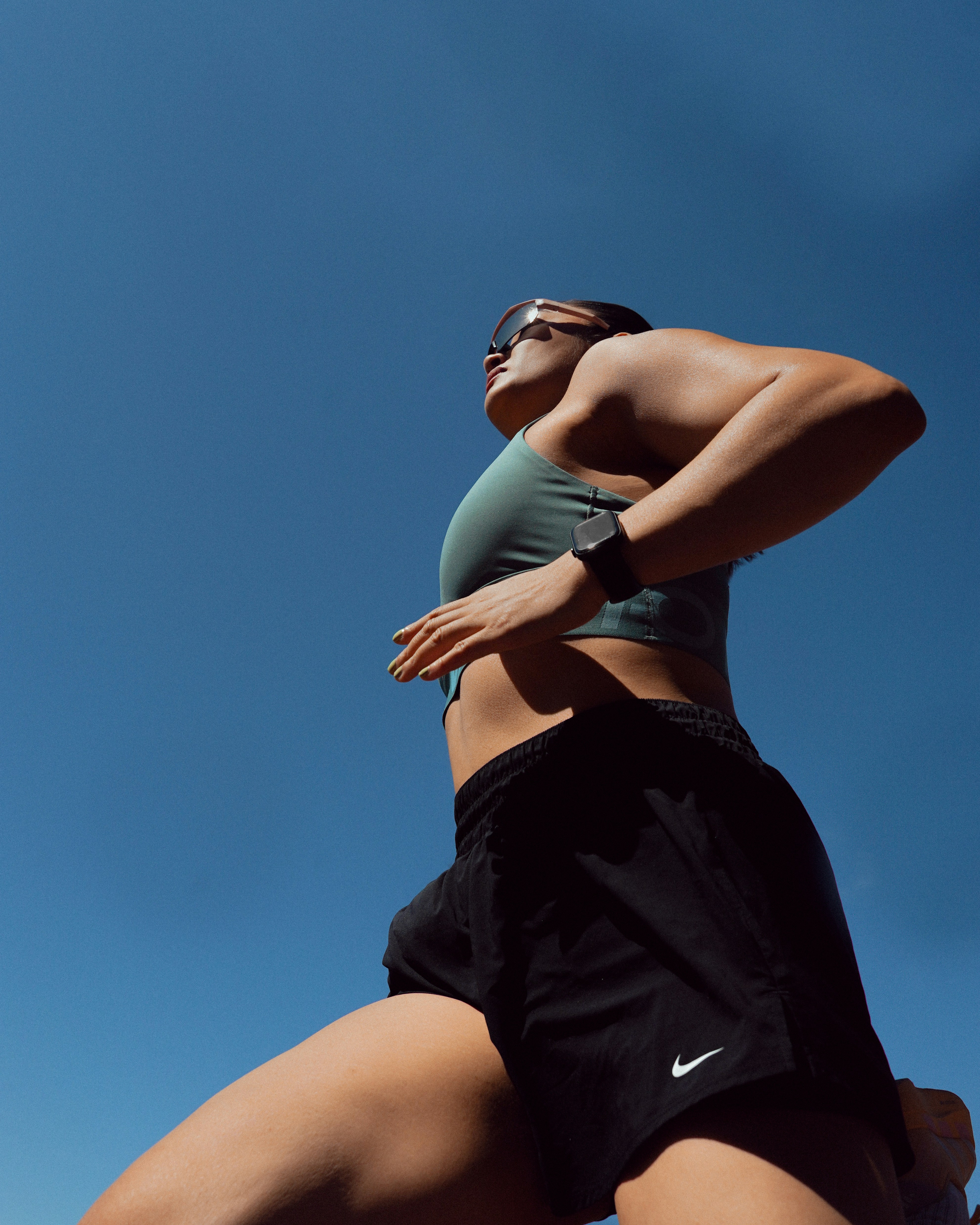 A woman running in a green sports bra and black shorts against blue sky