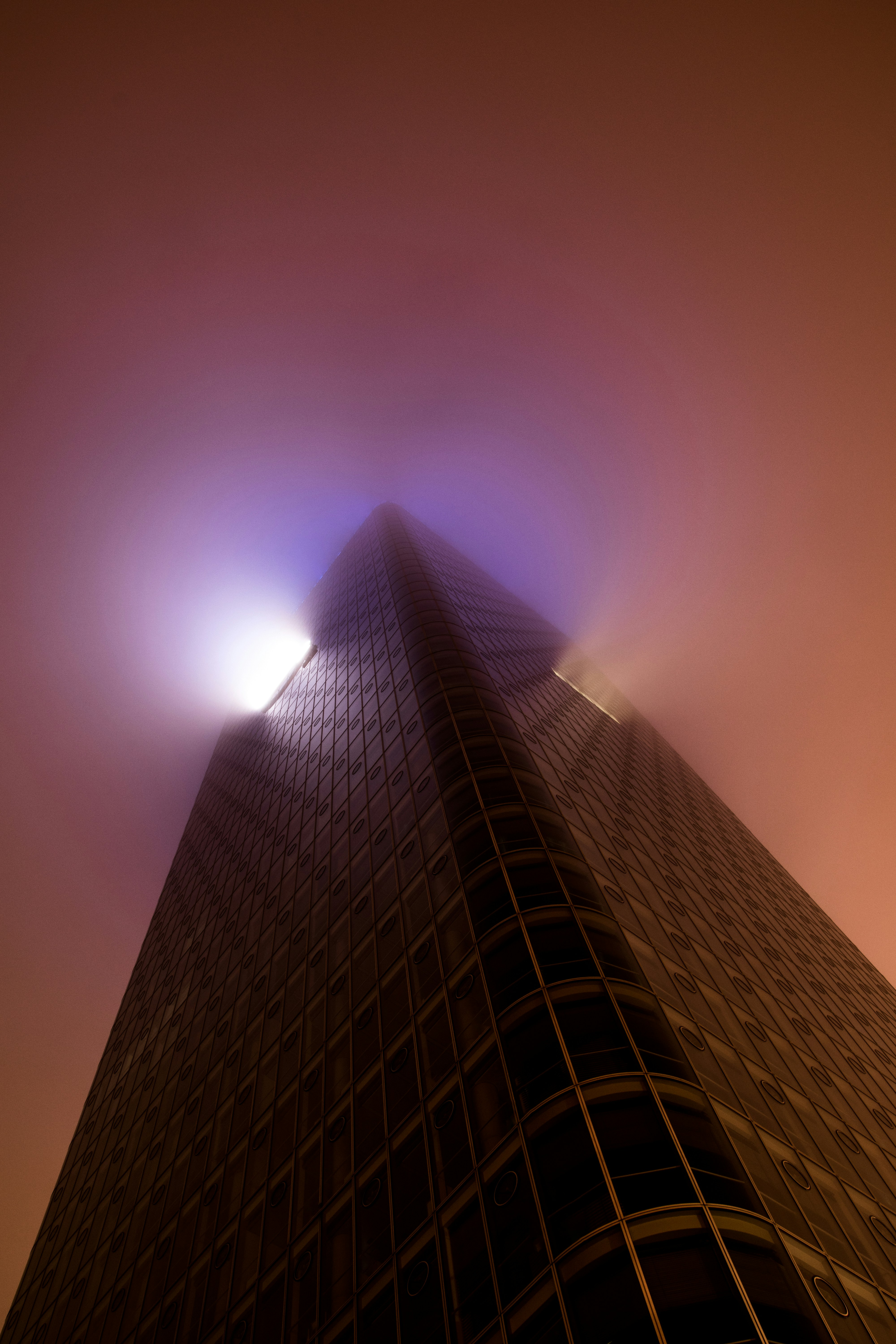 Eine Ecke eines Wolkenkratzers verschwindet in dichtem orangefarbenem Nebel mit einem hellblauen Licht