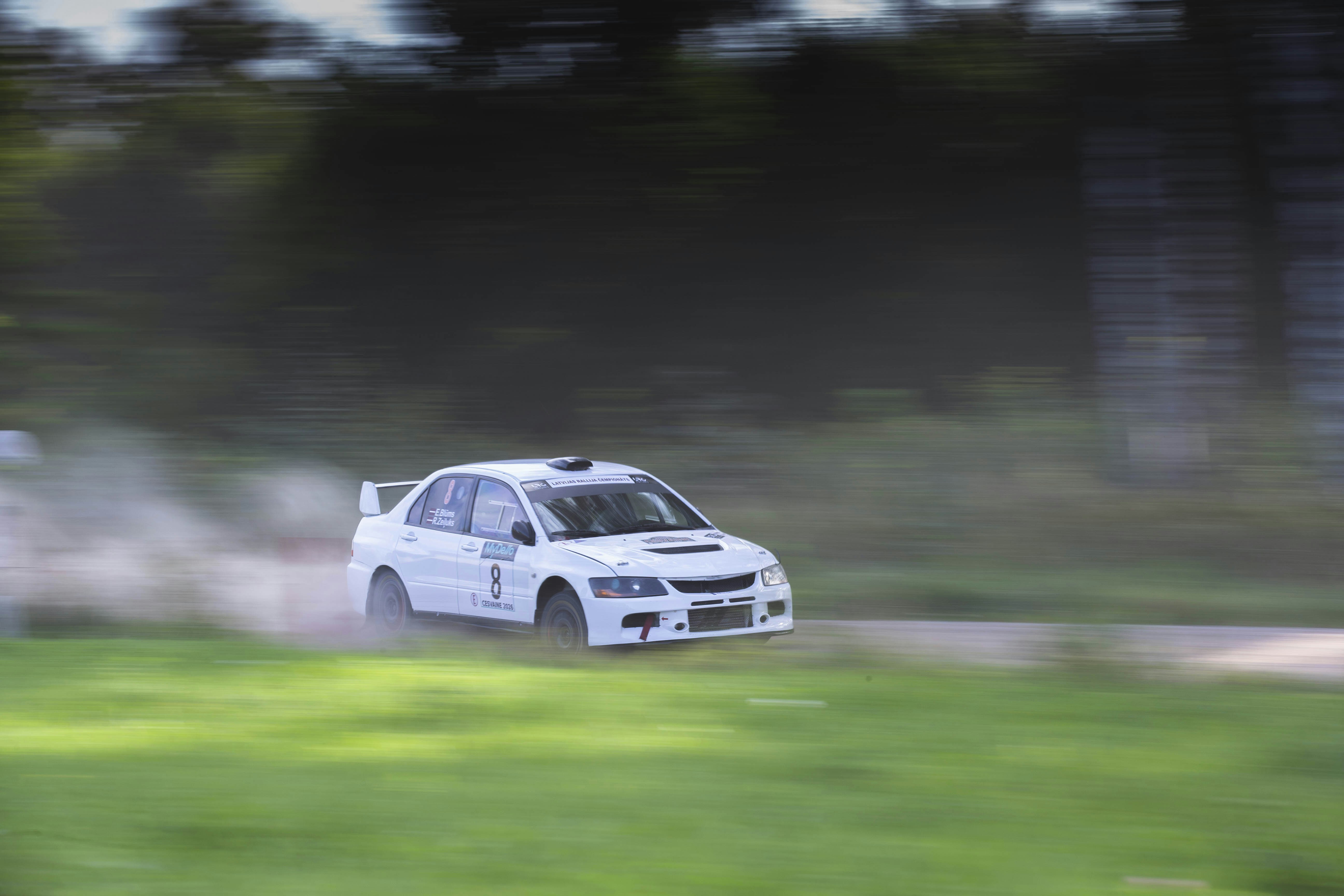 A white rally car speeding along a dirt track with motion blur