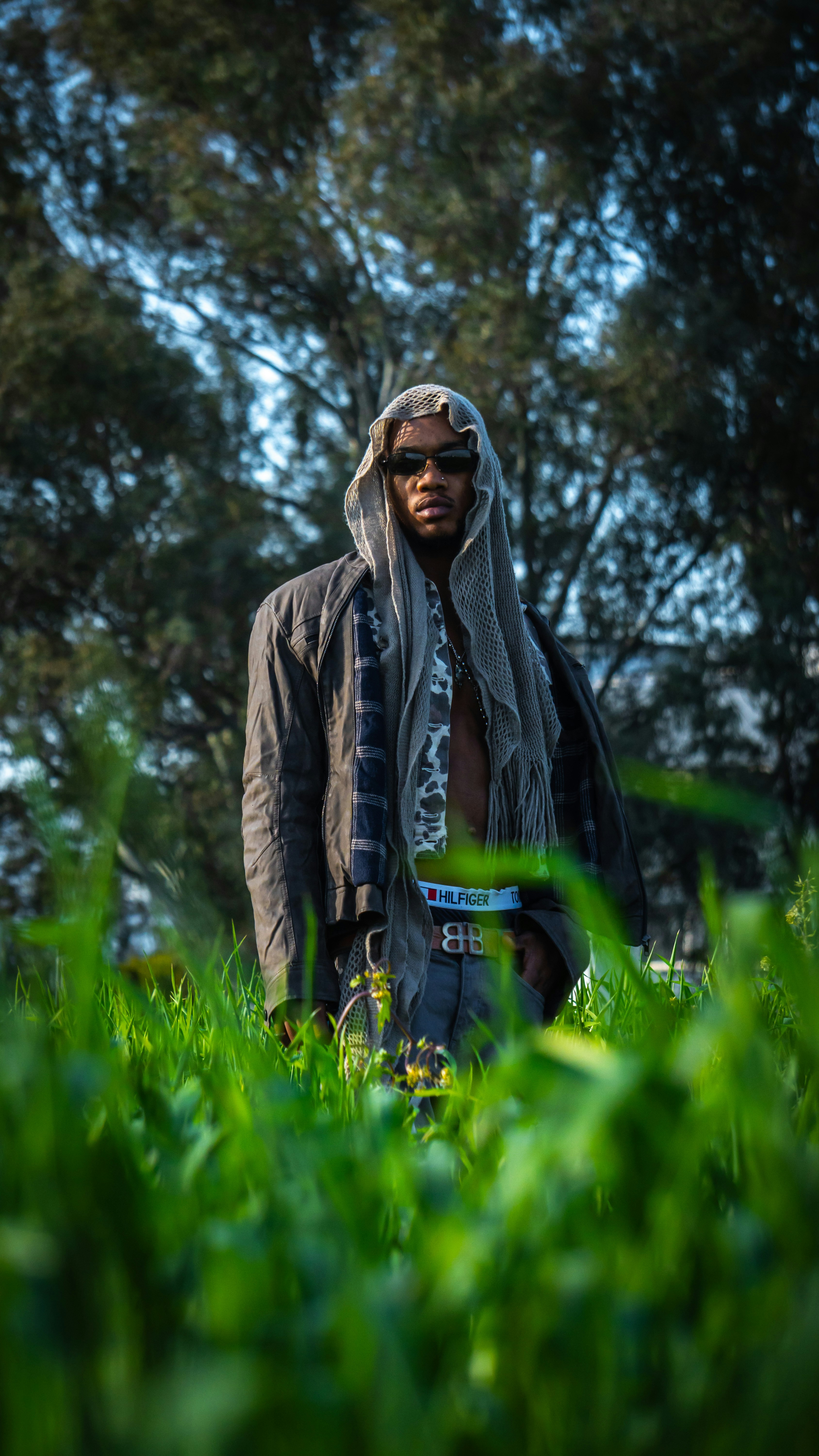 A person in a hooded scarf and jacket standing in a grassy field