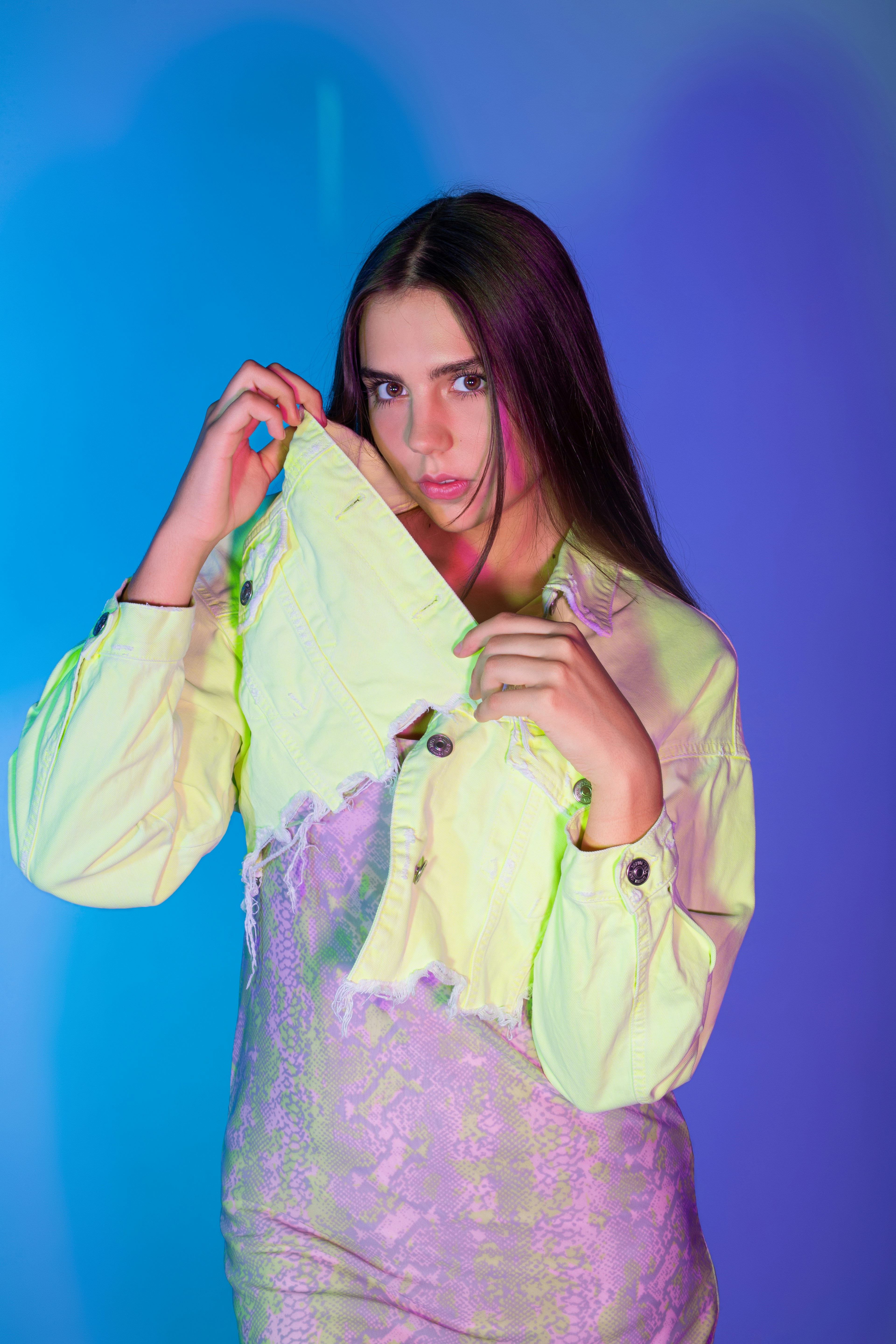 A woman in a neon yellow cropped denim jacket over a patterned dress