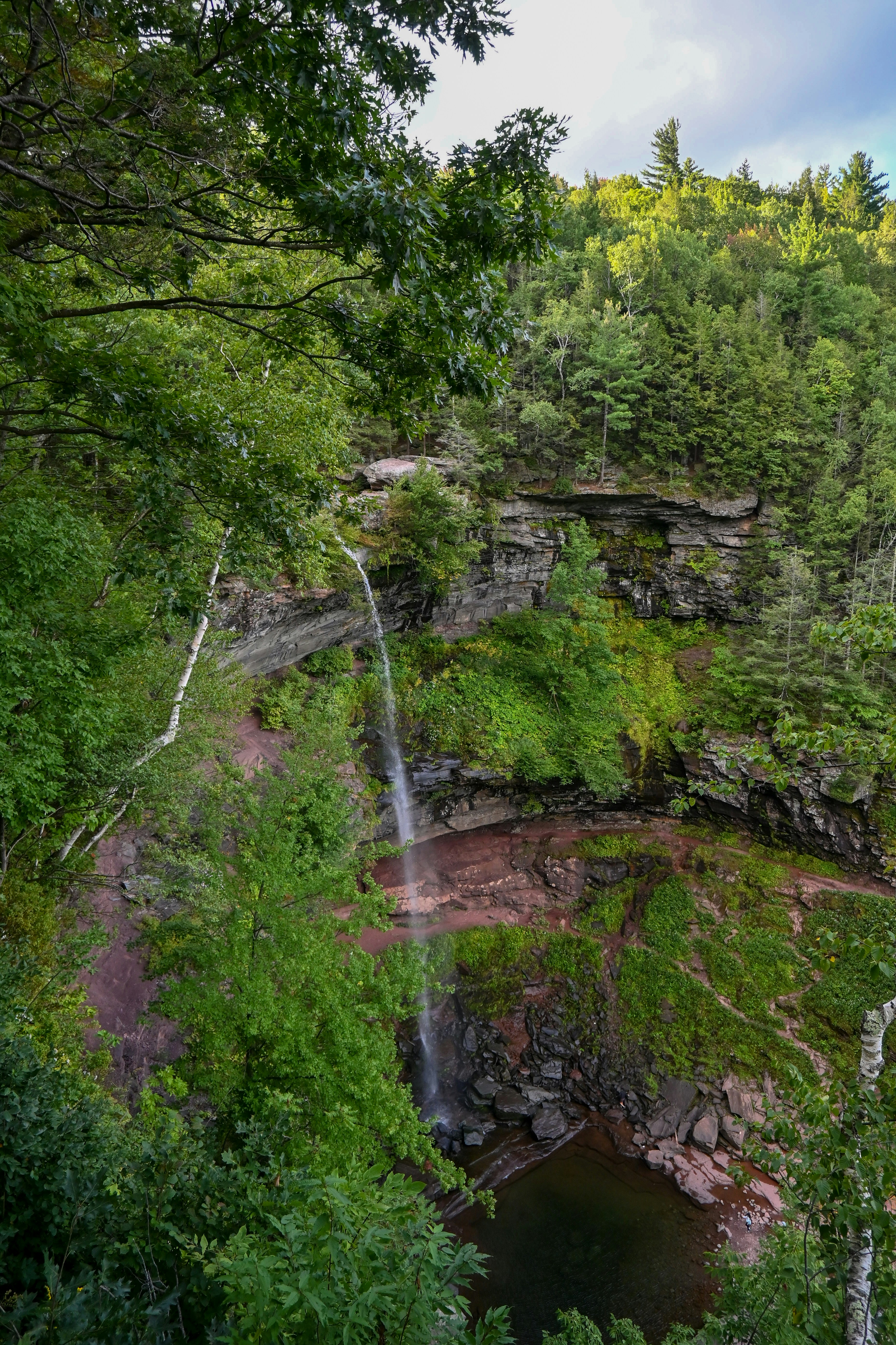 Una sottile cascata che scende su una scogliera rocciosa fino a una pozza sottostante