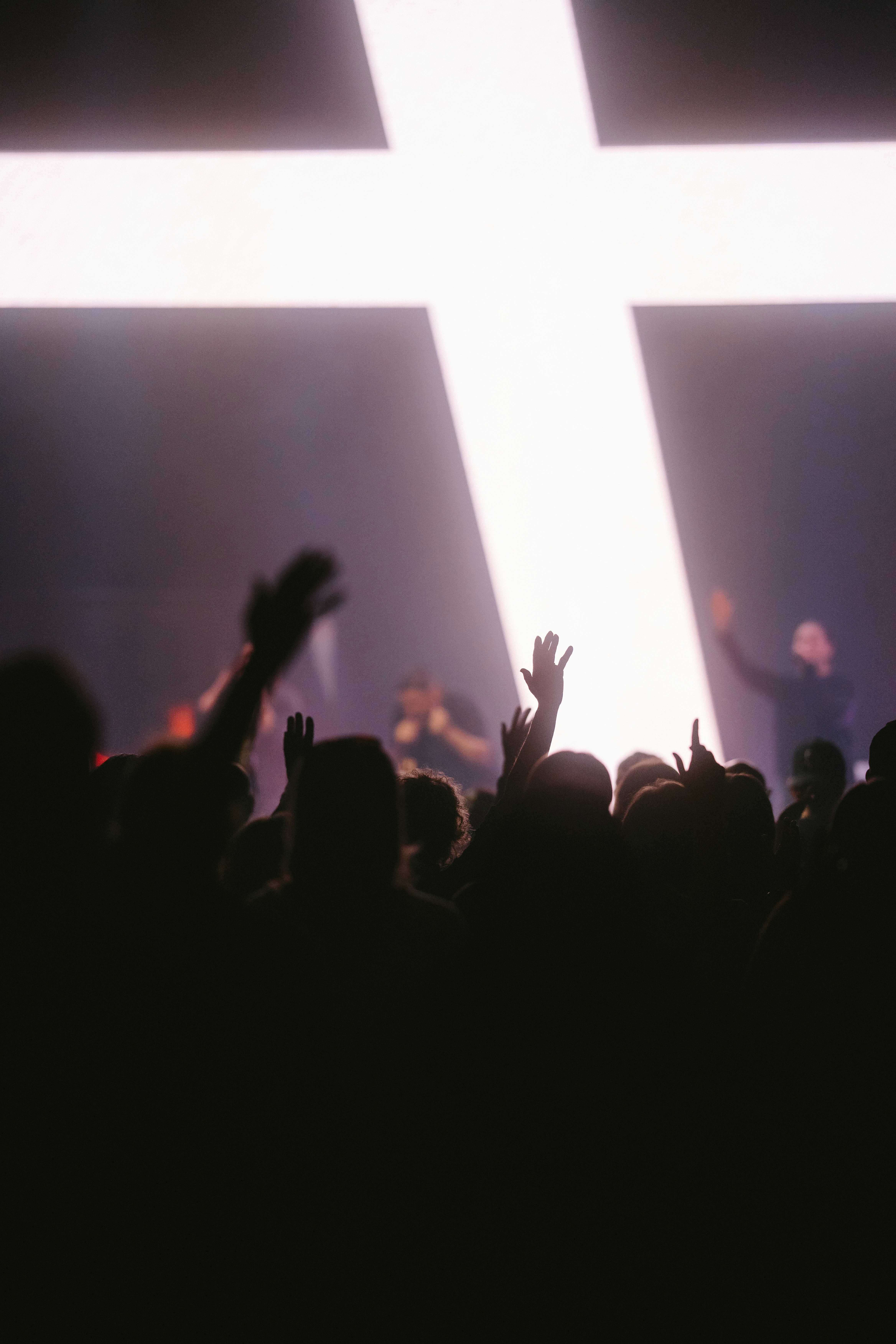 A crowd of people with raised hands before a large glowing cross