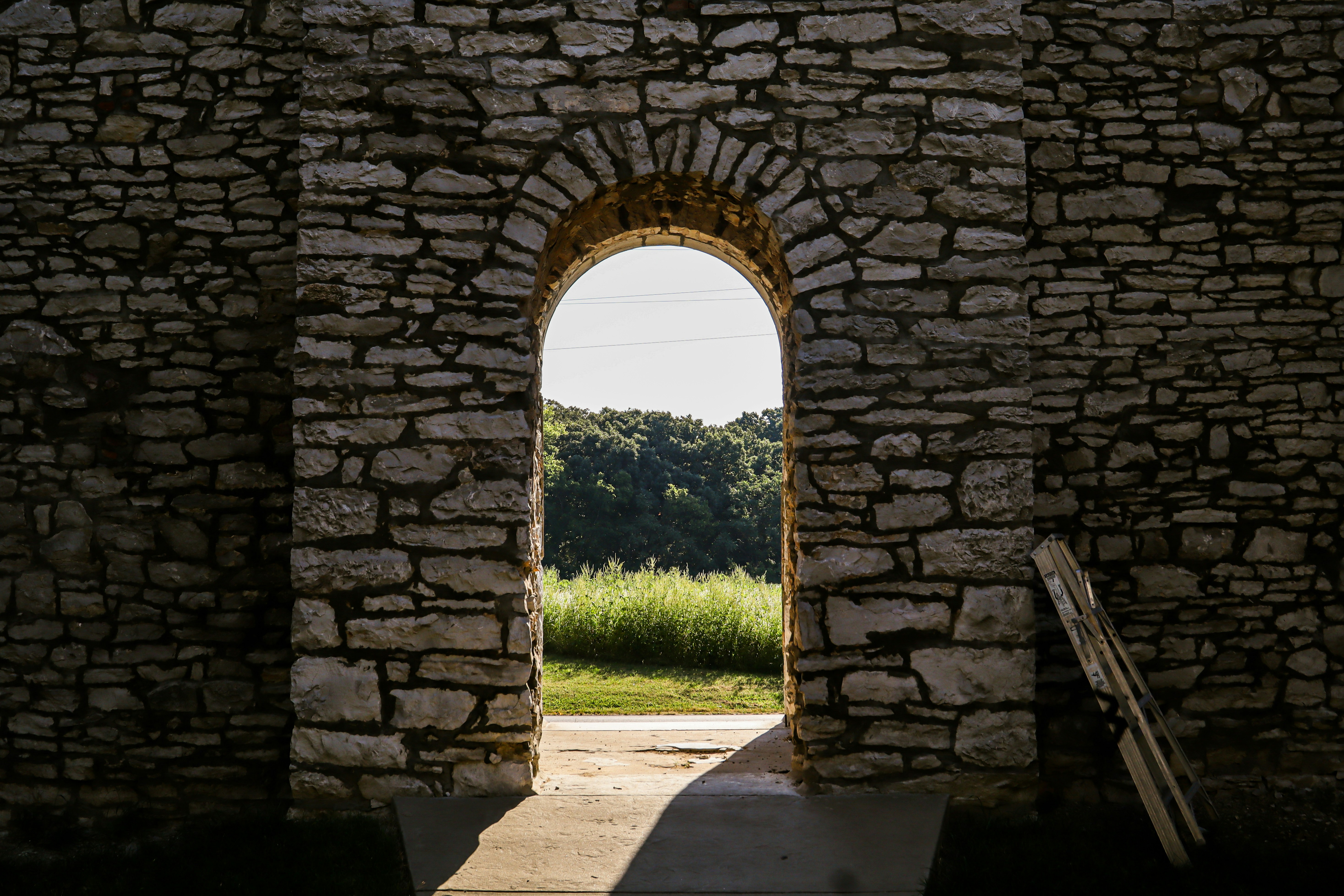A stone archway framing a view of a green field and trees