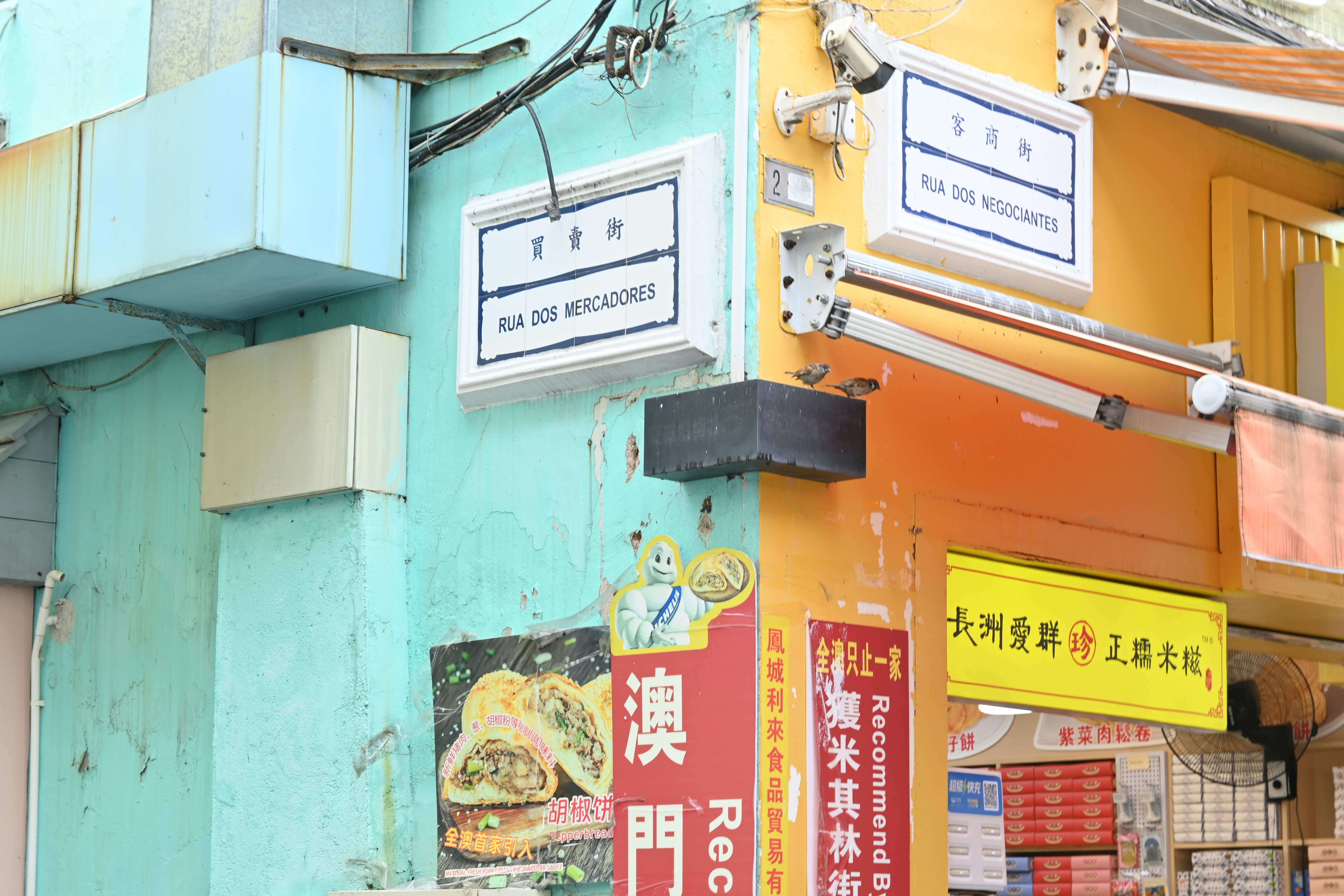 Street signs in Chinese and Portuguese on a corner building in Macau, above shop signs in Chinese and English