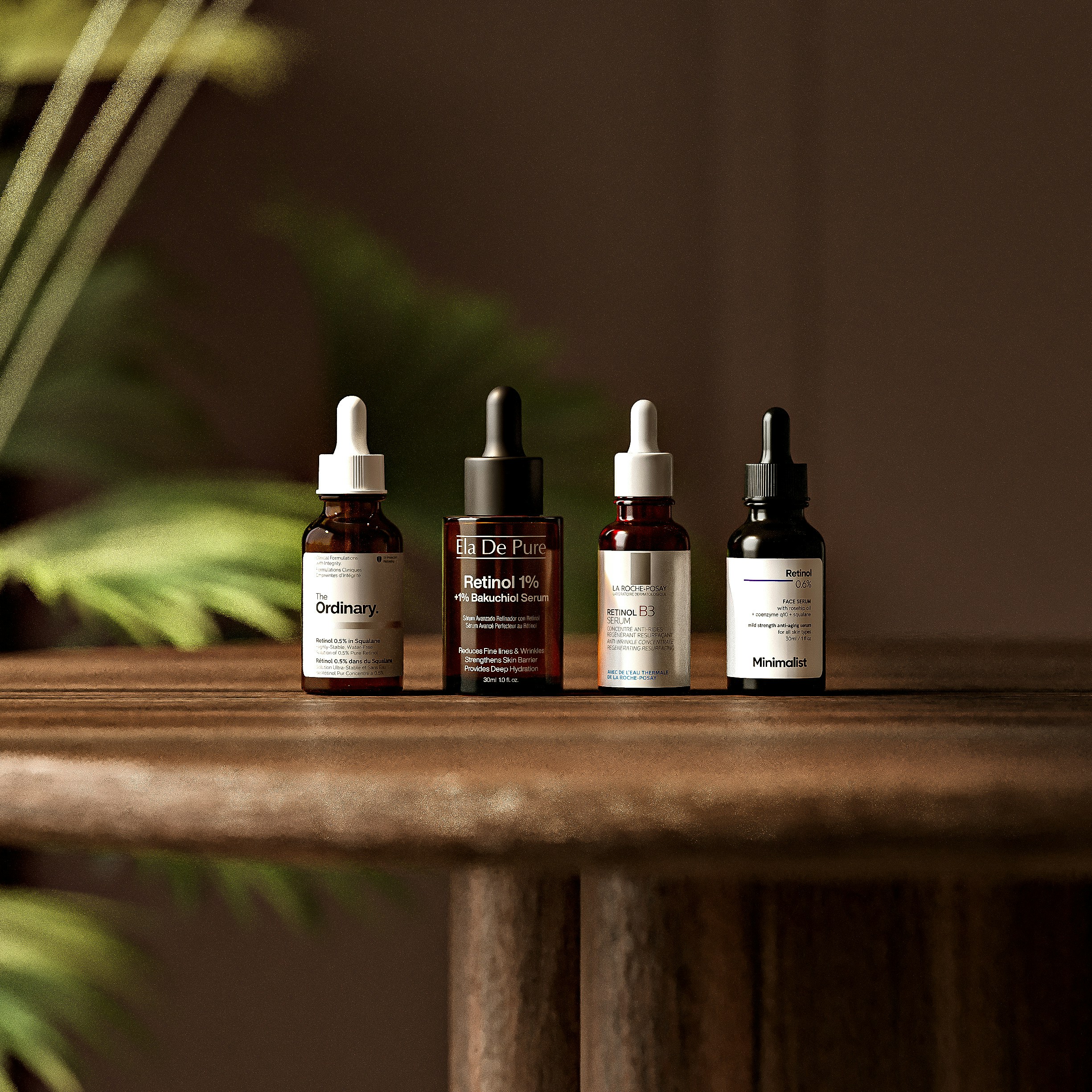 Four glass dropper bottles of skincare serum on a wooden table with a plant