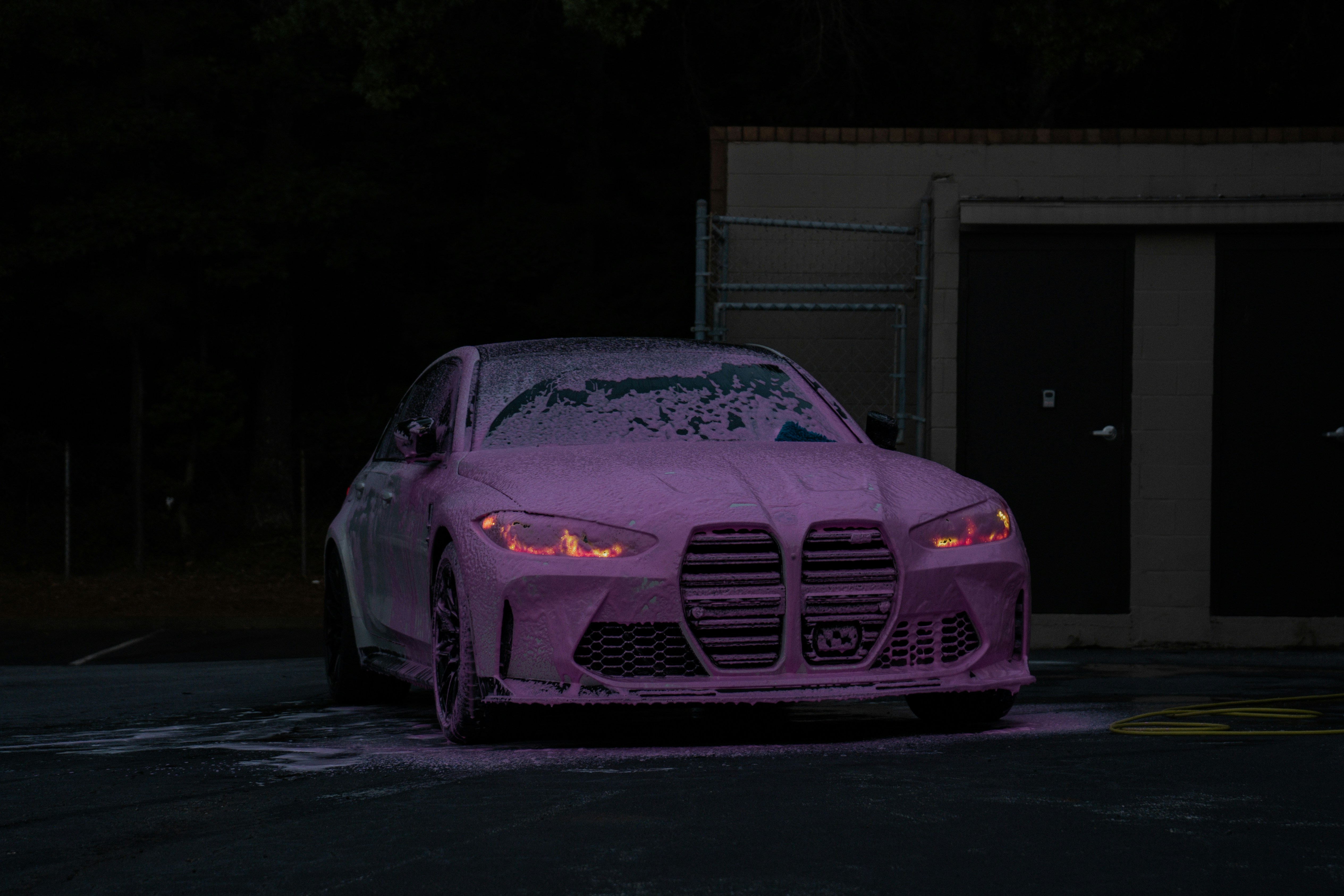 A car covered in pink soap suds with glowing orange headlights at night