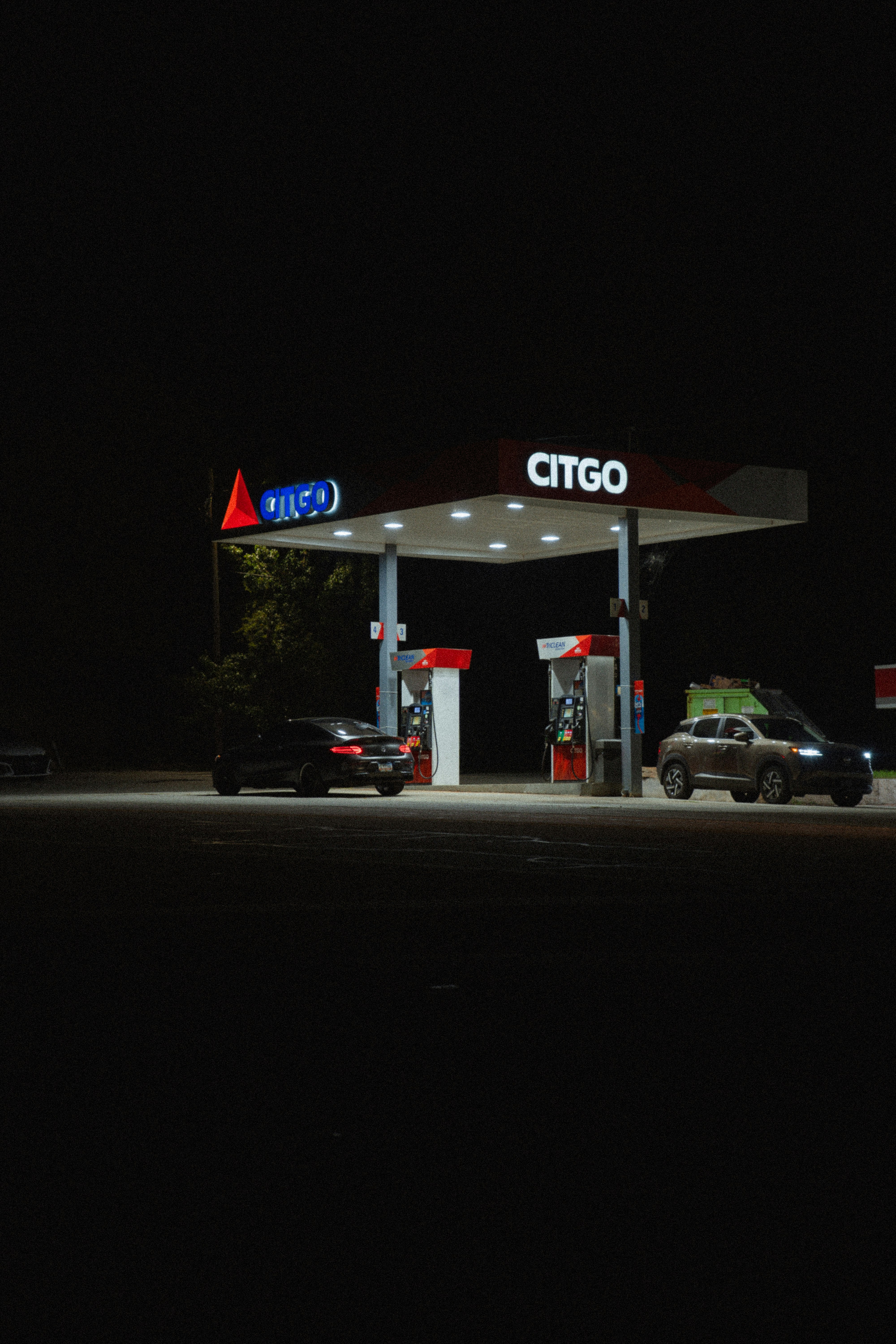 Two cars parked under a brightly lit Citgo gas station canopy at night
