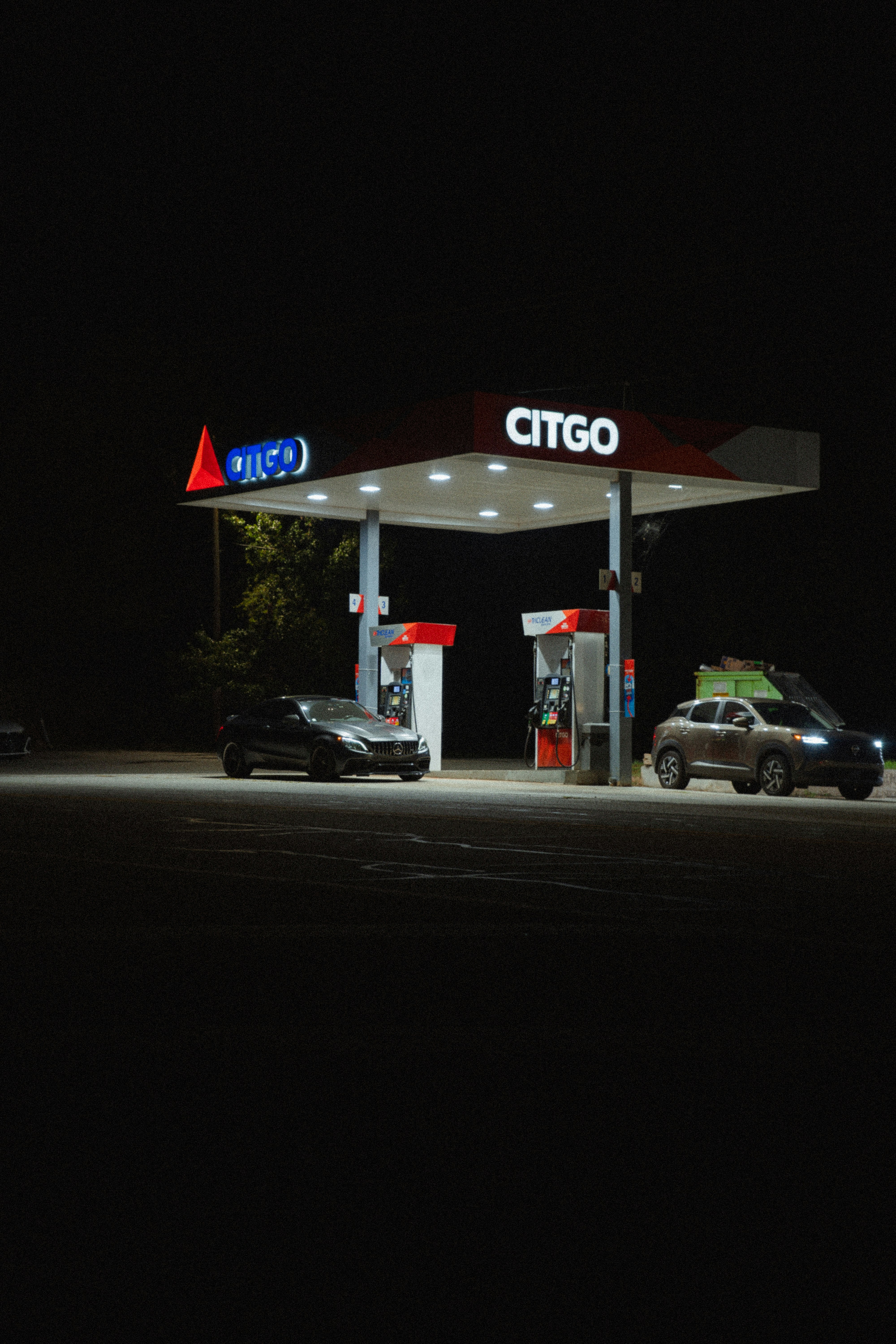 Two cars parked under a brightly lit Citgo gas station canopy at night