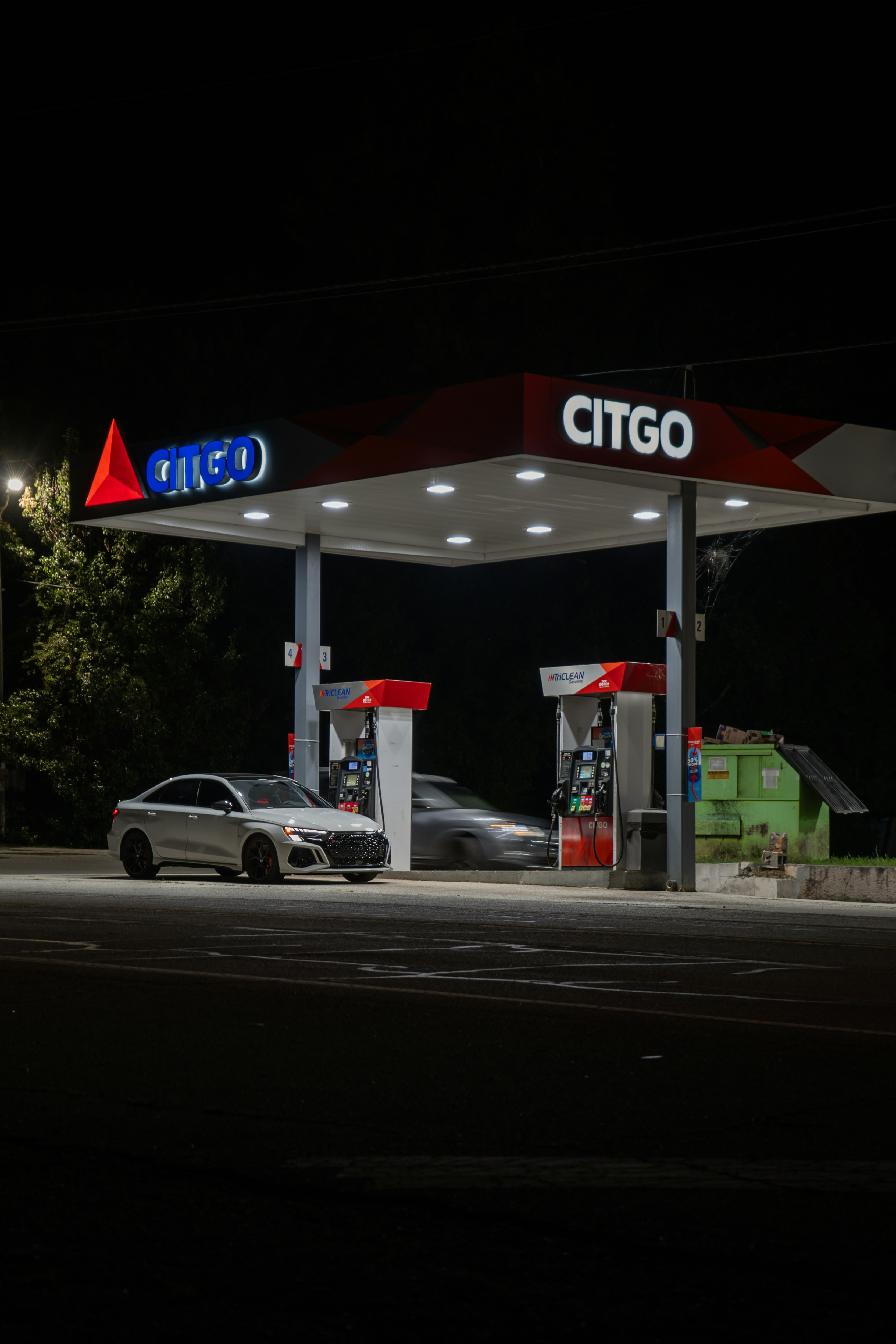 A white sedan parked at a Citgo gas station at night under bright lights