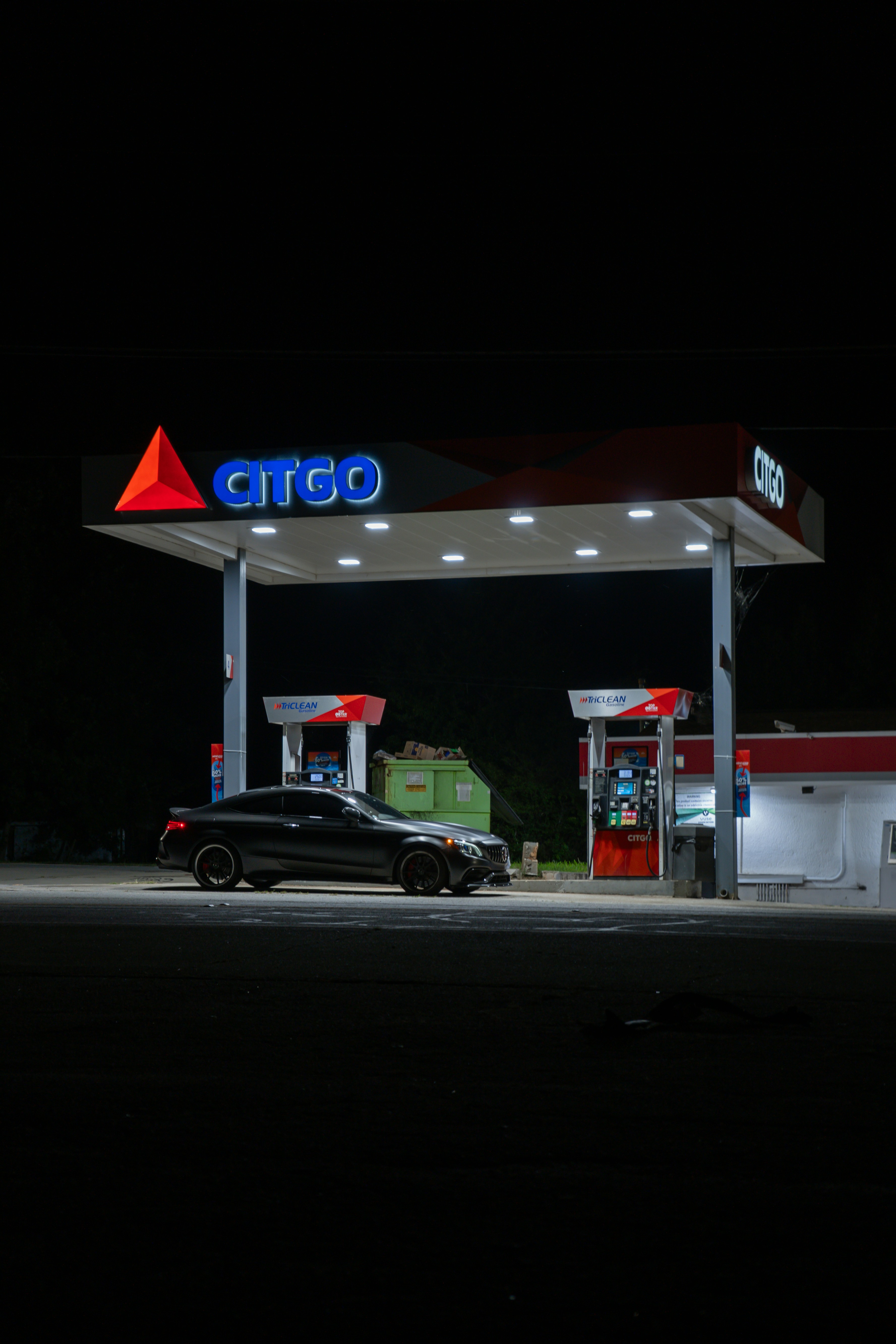 A dark grey coupe parked under a brightly lit Citgo gas station canopy at night