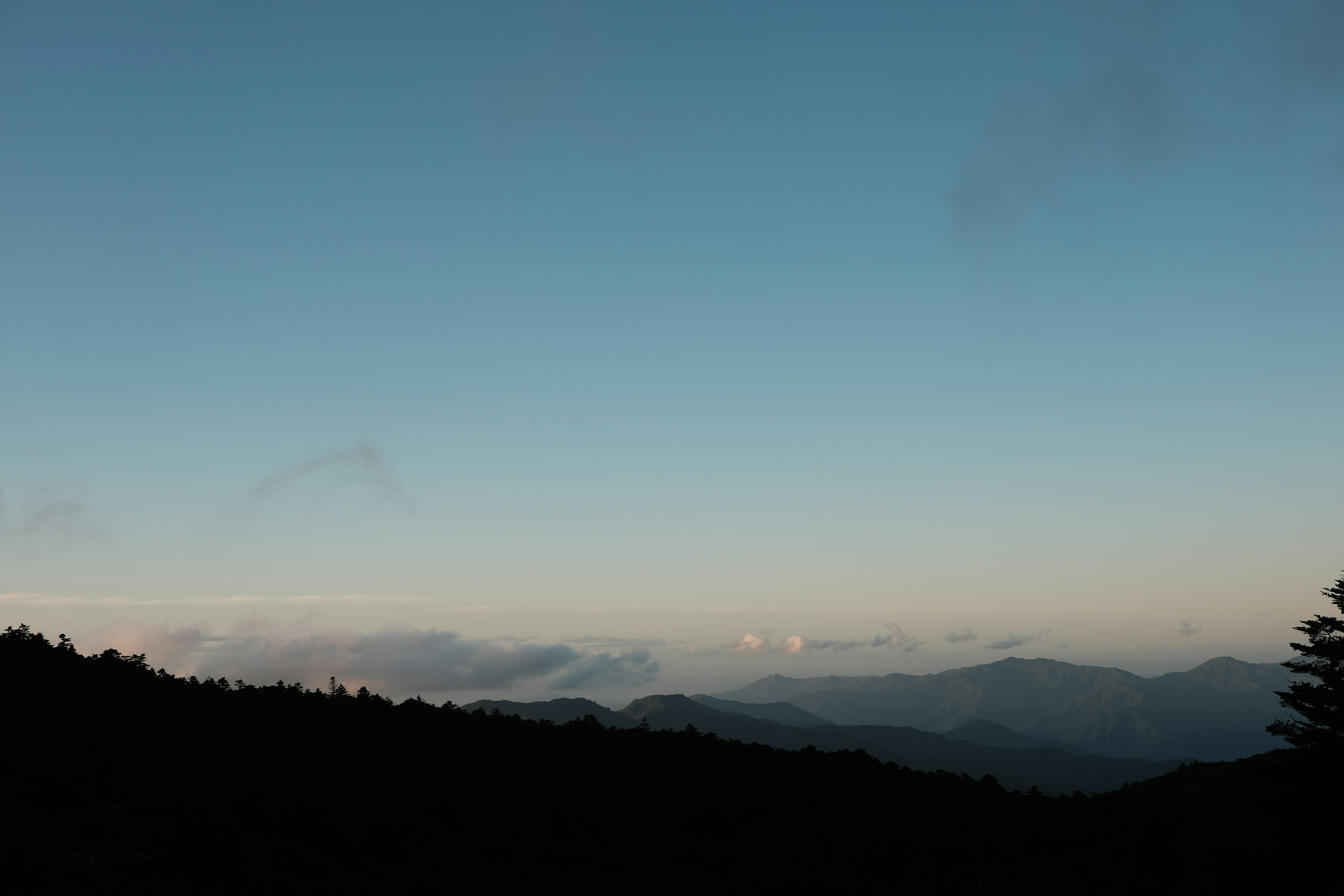 Silhouetted mountain ridges under a clear blue sky with distant low clouds