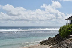 A tropical beach with rocky shore and a wooden structure under a cloudy sky