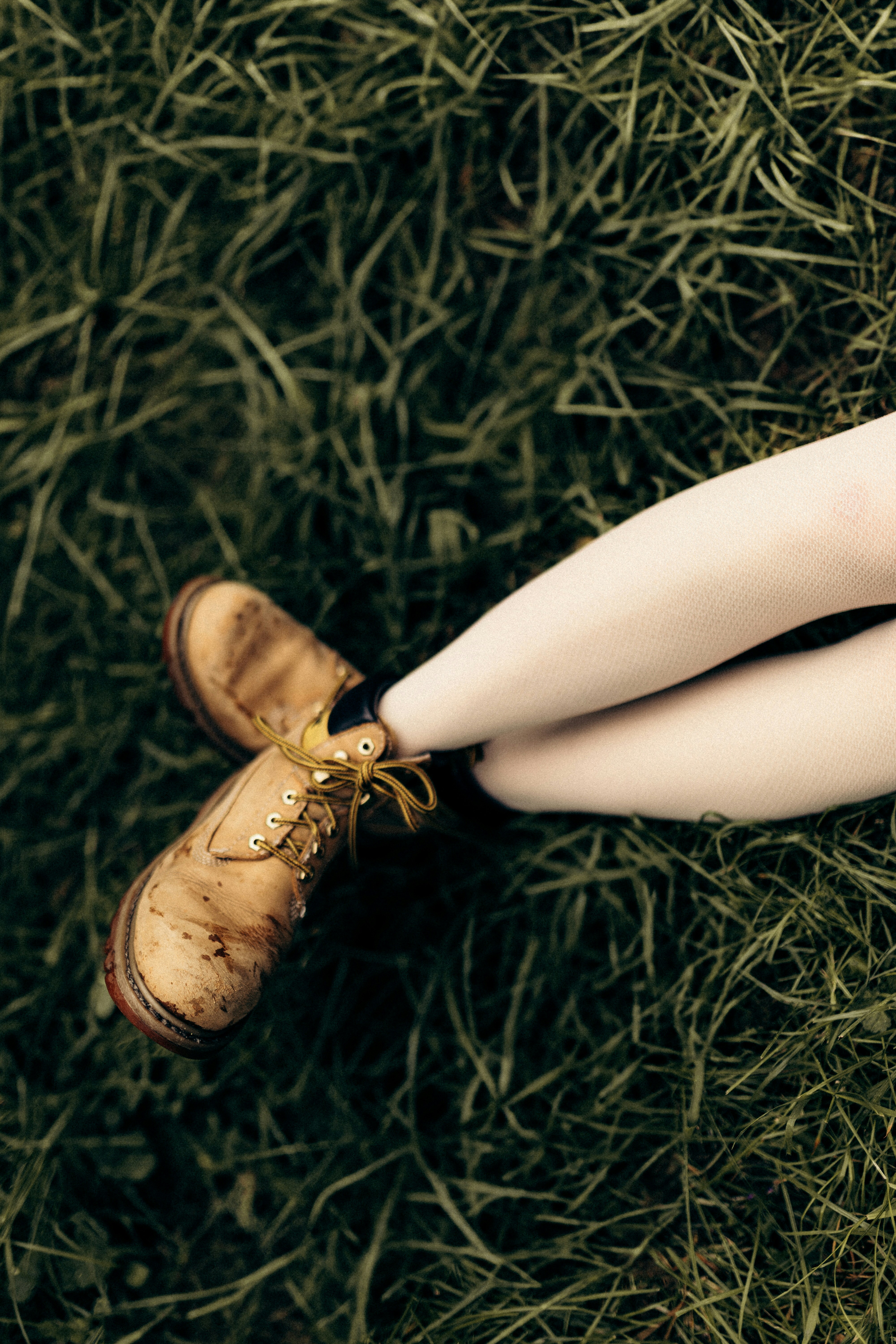 A person wearing white tights and worn tan work boots in green grass