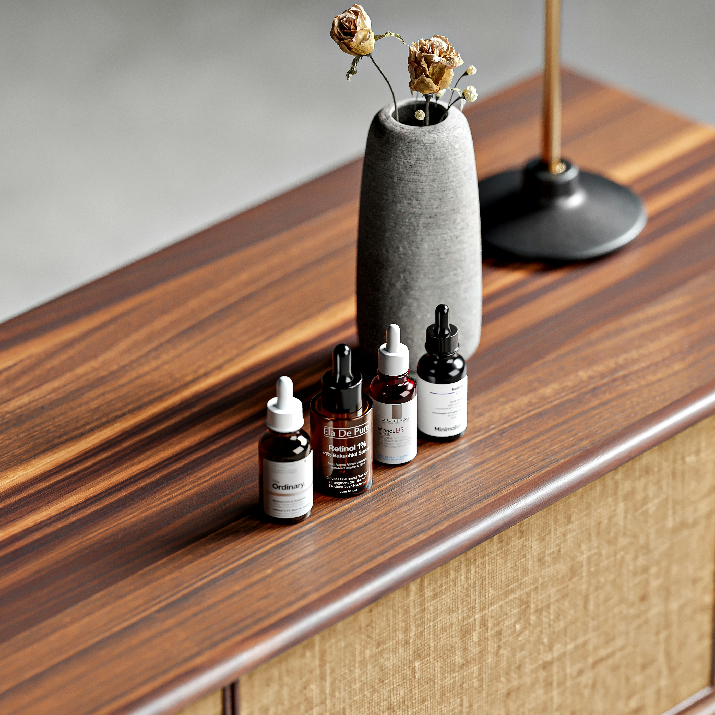 Four dropper bottles of skincare serum beside a stone vase on a wooden table