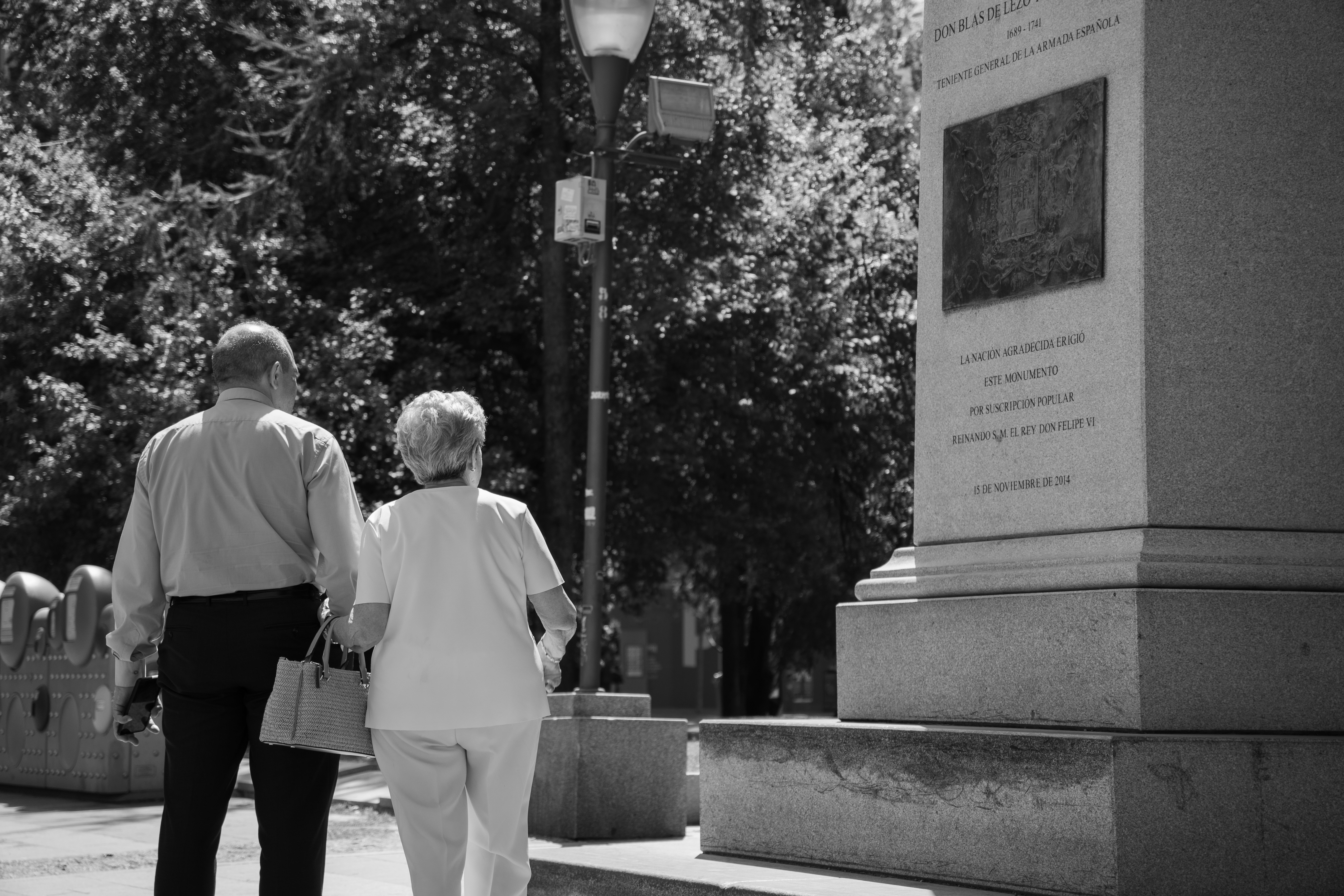 Two adults walking past a stone monument with an inscription in a park - monuments and memorials