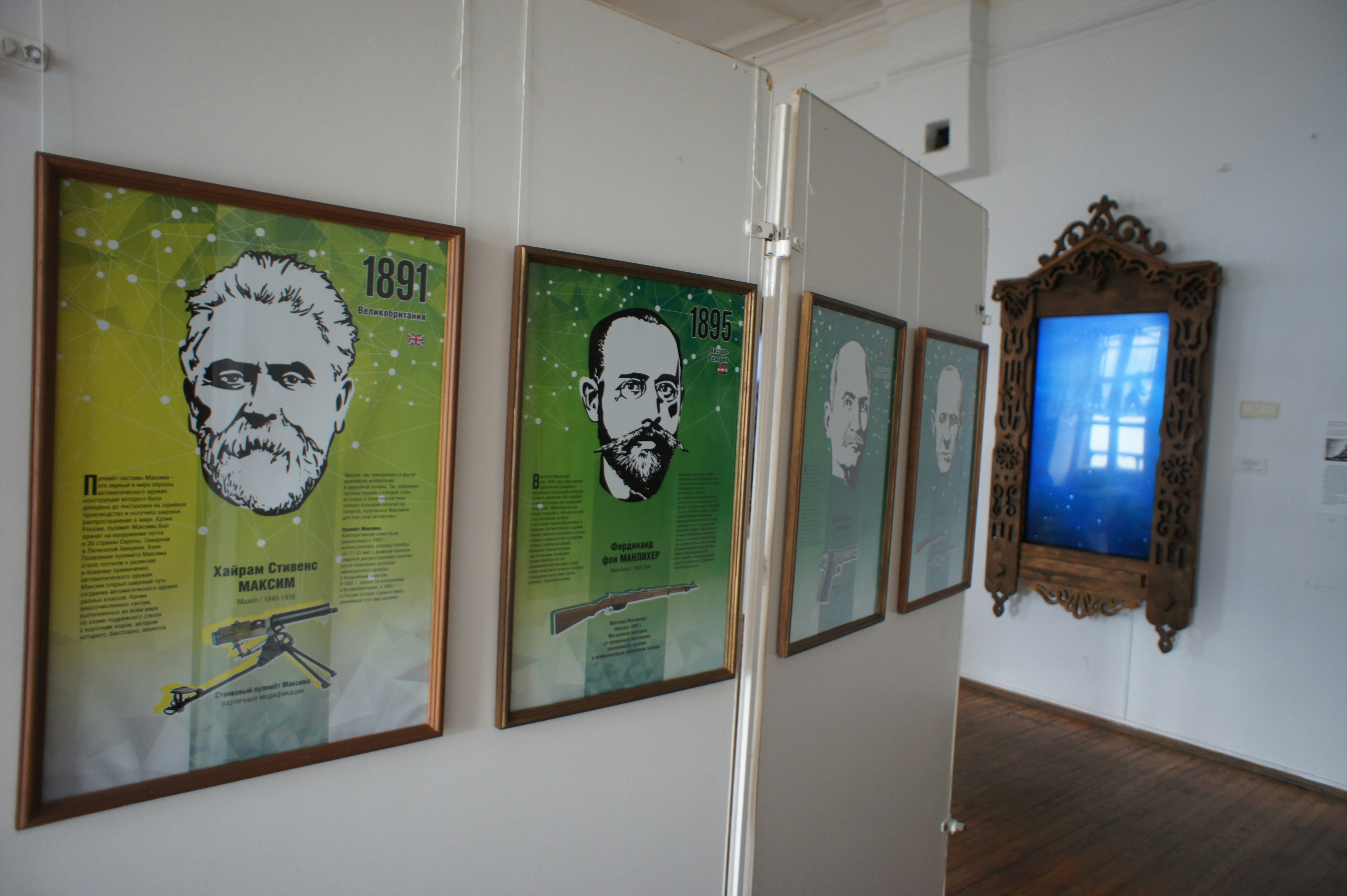 Framed posters of historical figures and weapons hanging on a white partition wall