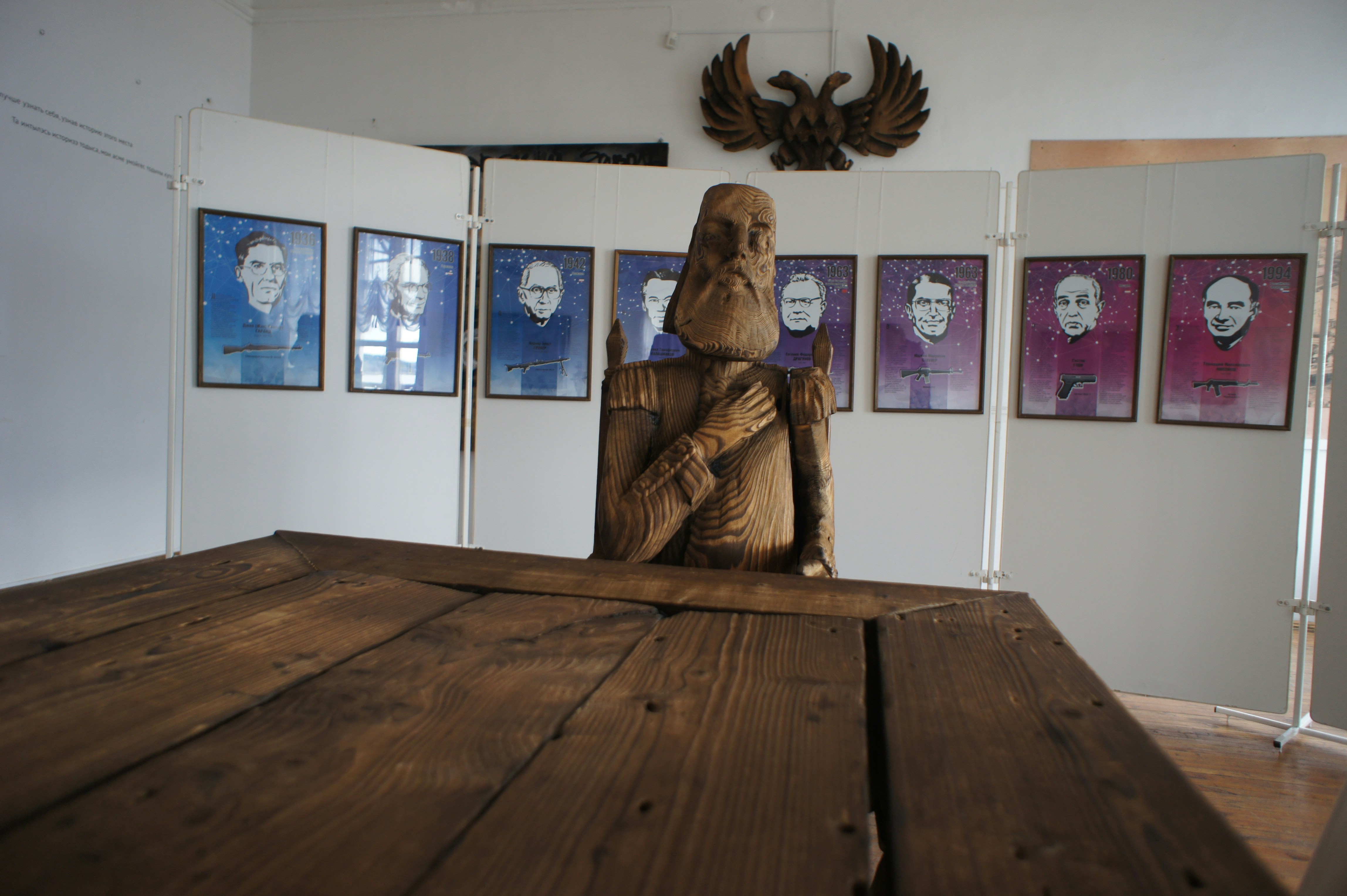 A wooden sculpture of a man behind a table in a gallery